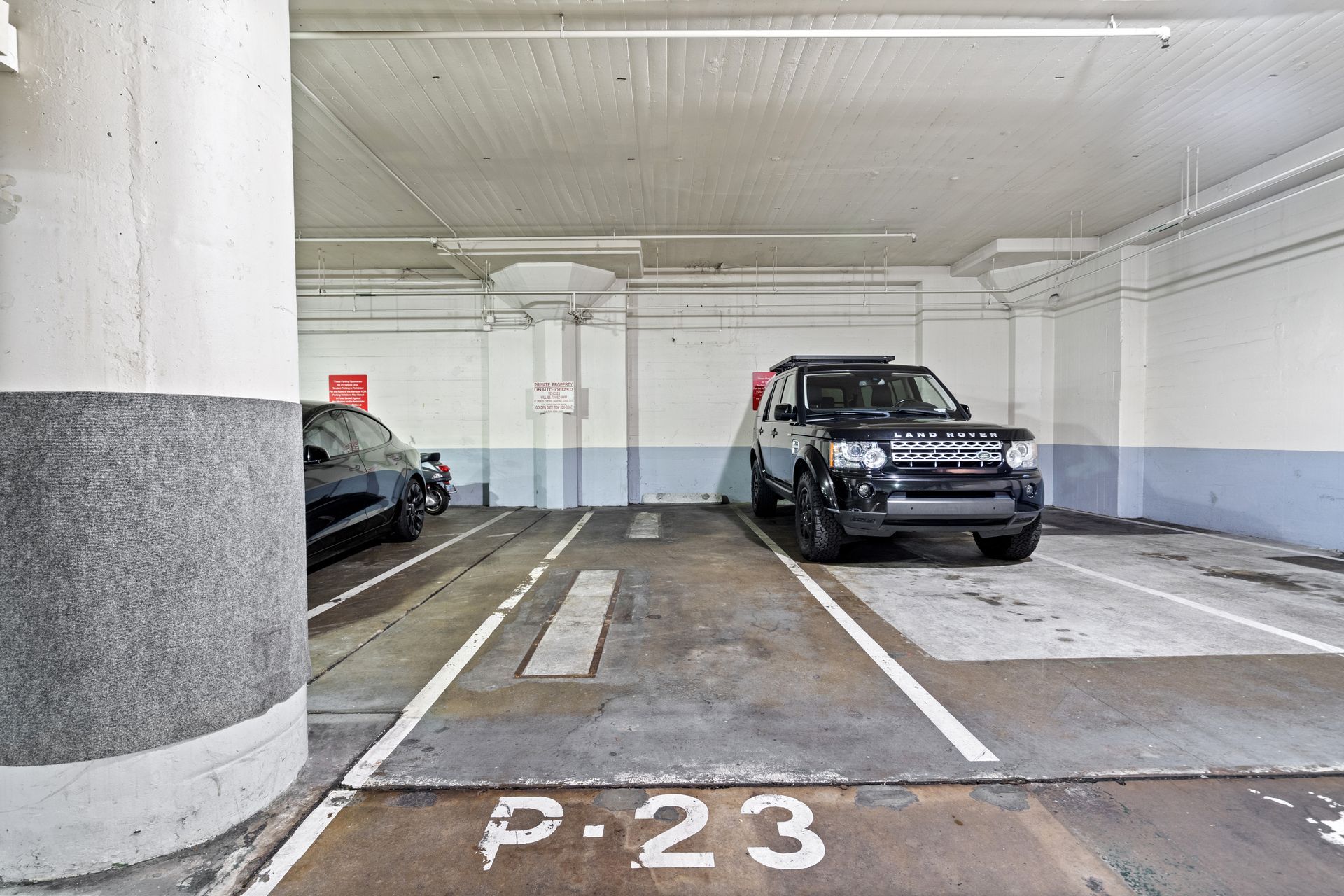 Parking garage with a black SUV and a car in adjacent spaces; a gray pillar is in the foreground.