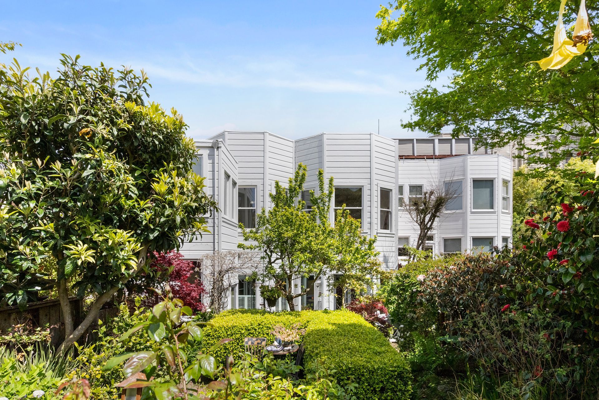 A large white house is surrounded by trees and bushes in a garden.