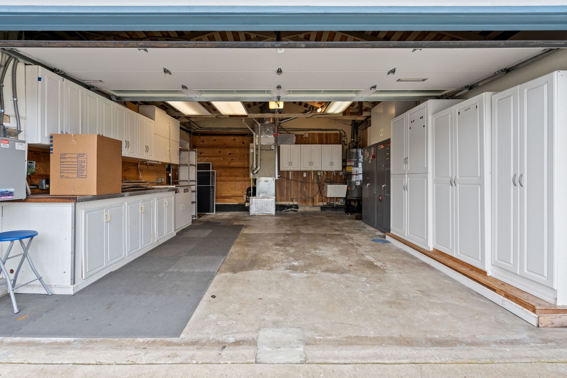 An empty garage with white cabinets and a stool.