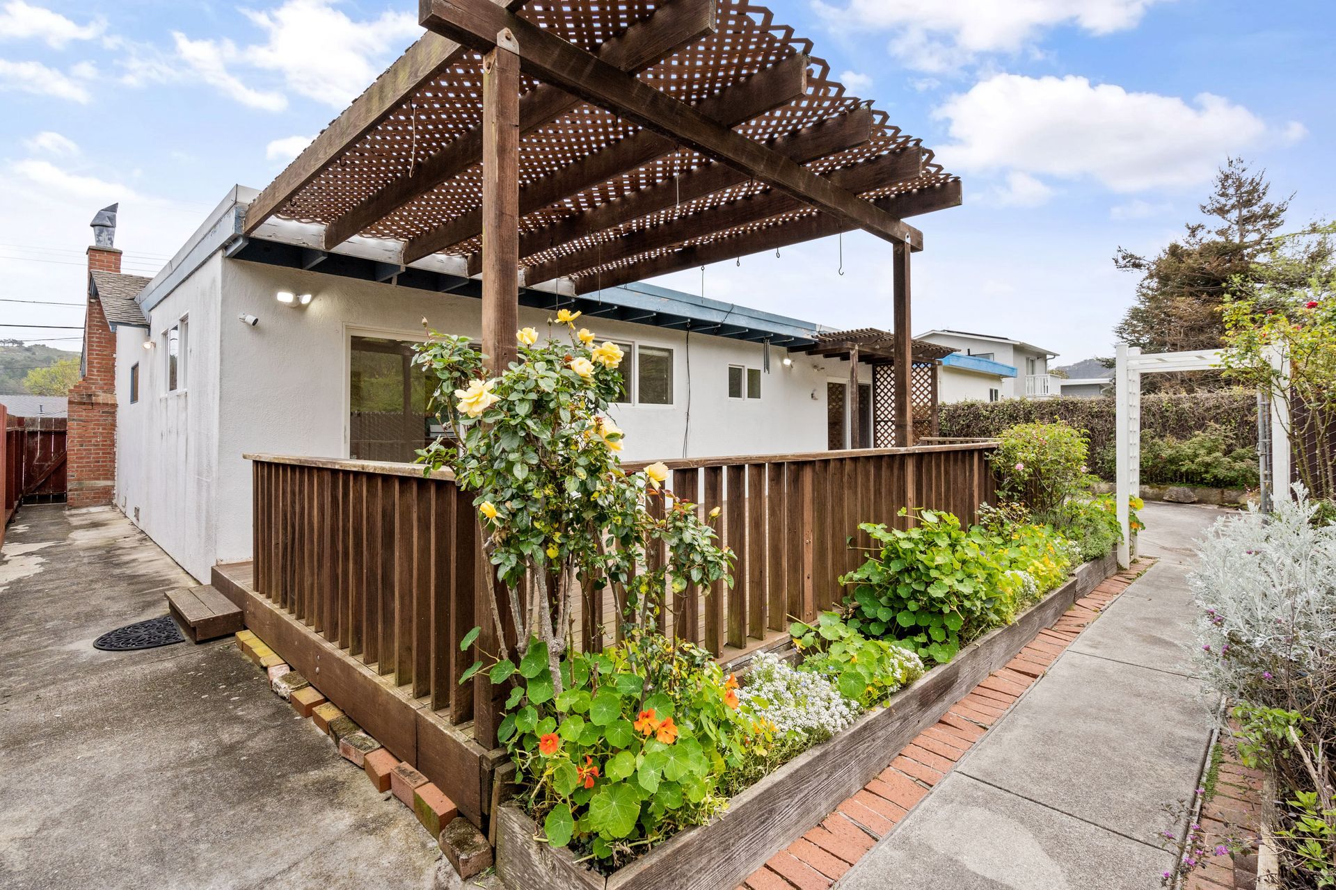A white house with a pergola and a garden in front of it.
