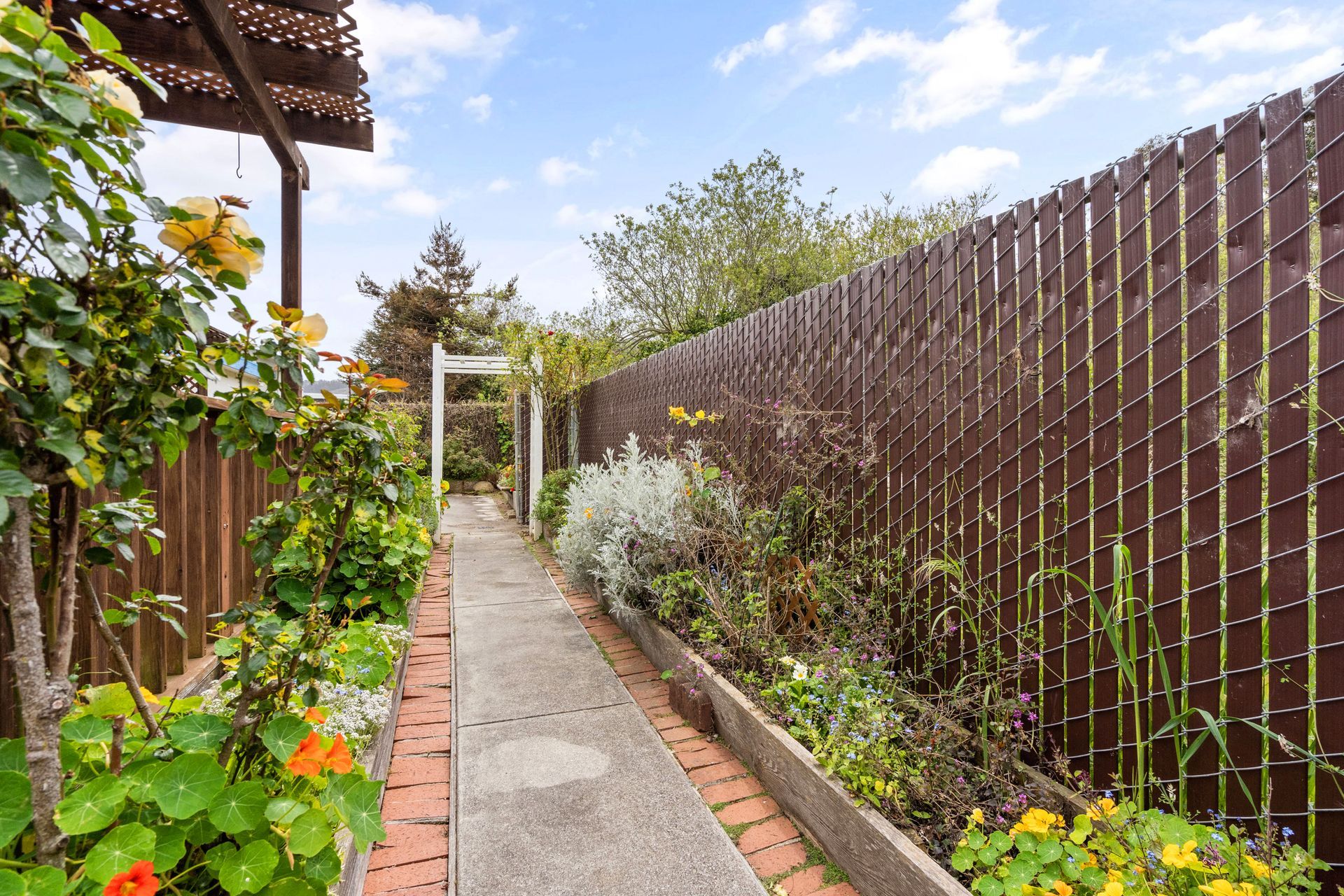 A brick walkway leading to a wooden fence in a garden.