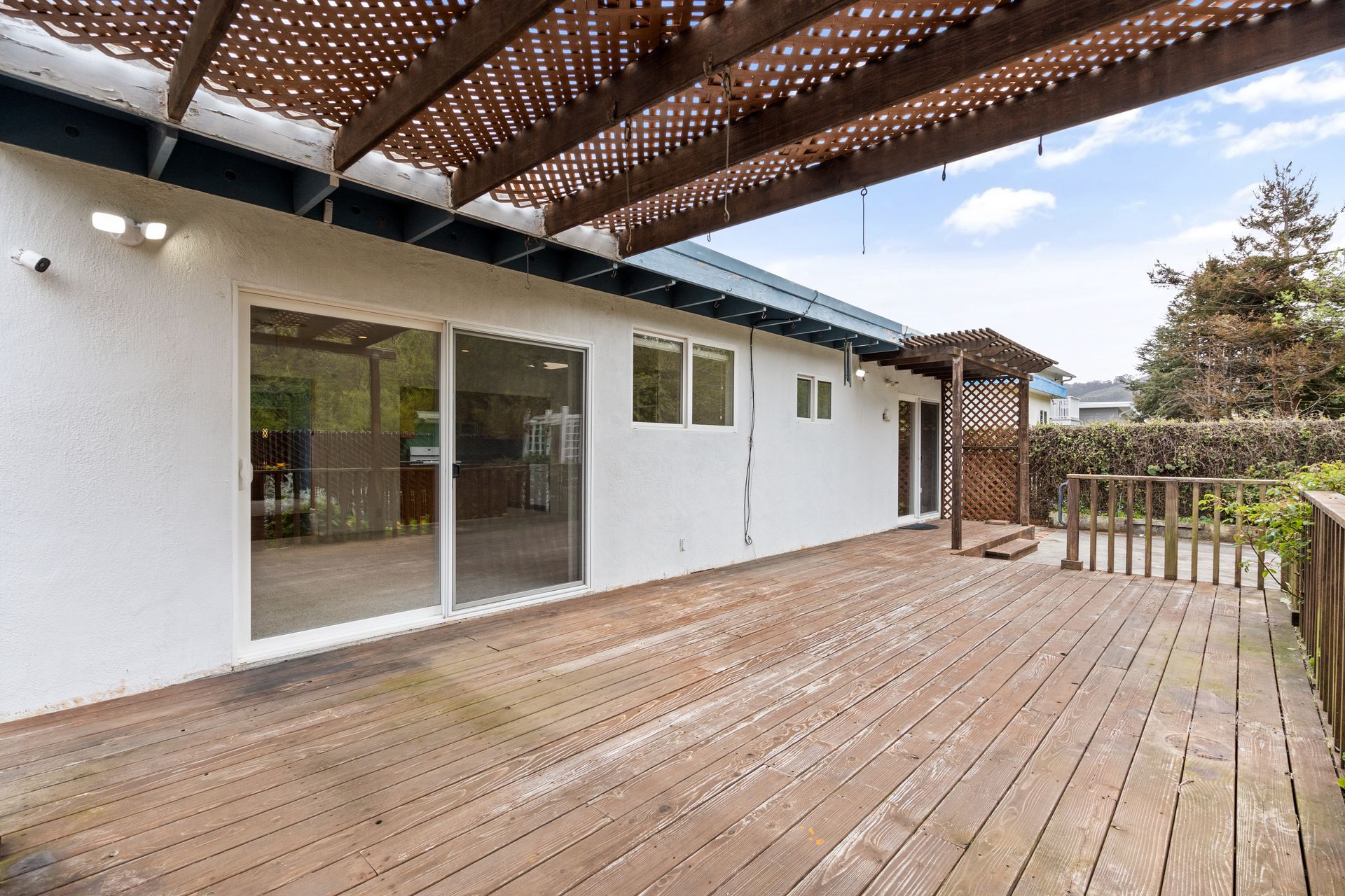 There is a wooden deck in front of a house with a pergola.