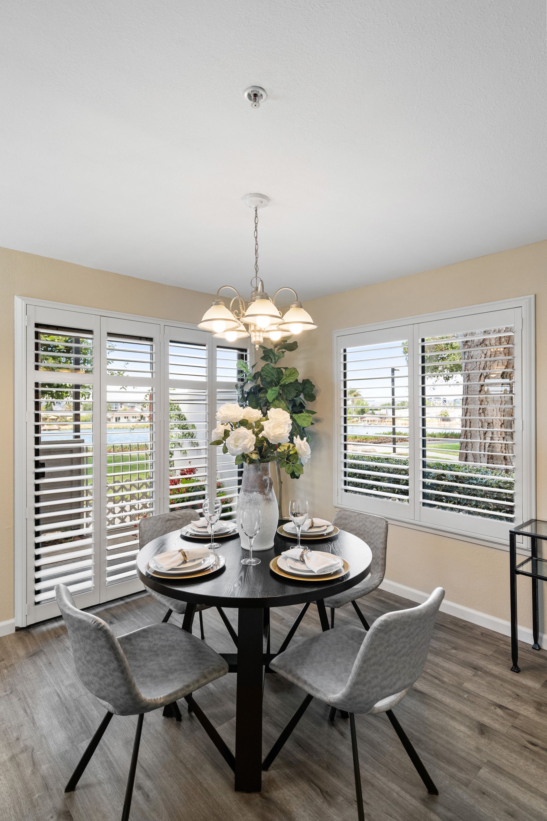 A dining room with a table and chairs and a vase of flowers on the table.