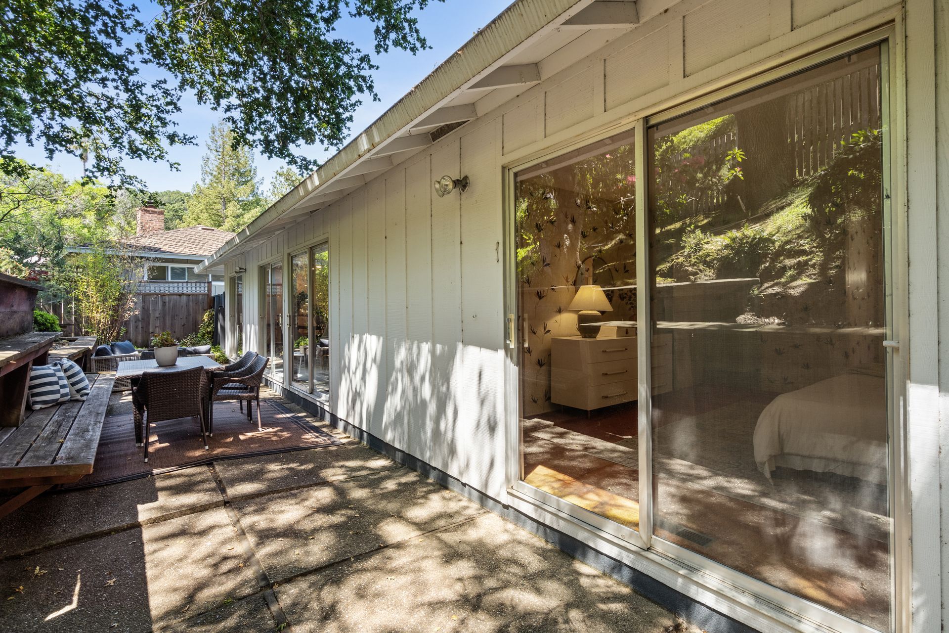 Exterior of a light-colored house with sliding glass doors opening to a patio with outdoor furniture.