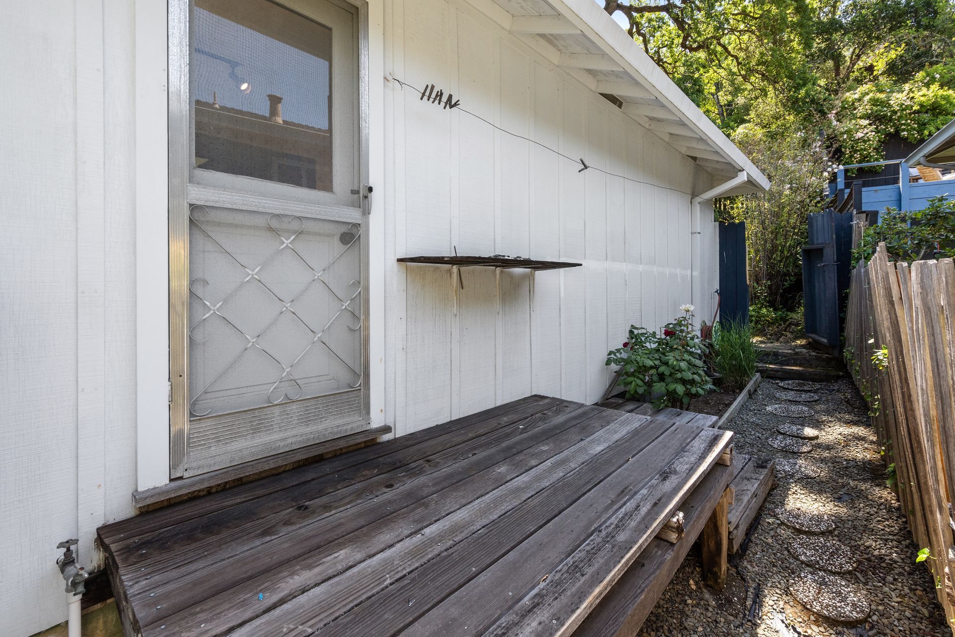 Side view of the house with a wooden deck and a pathway with stepping stones leading to a fence.
