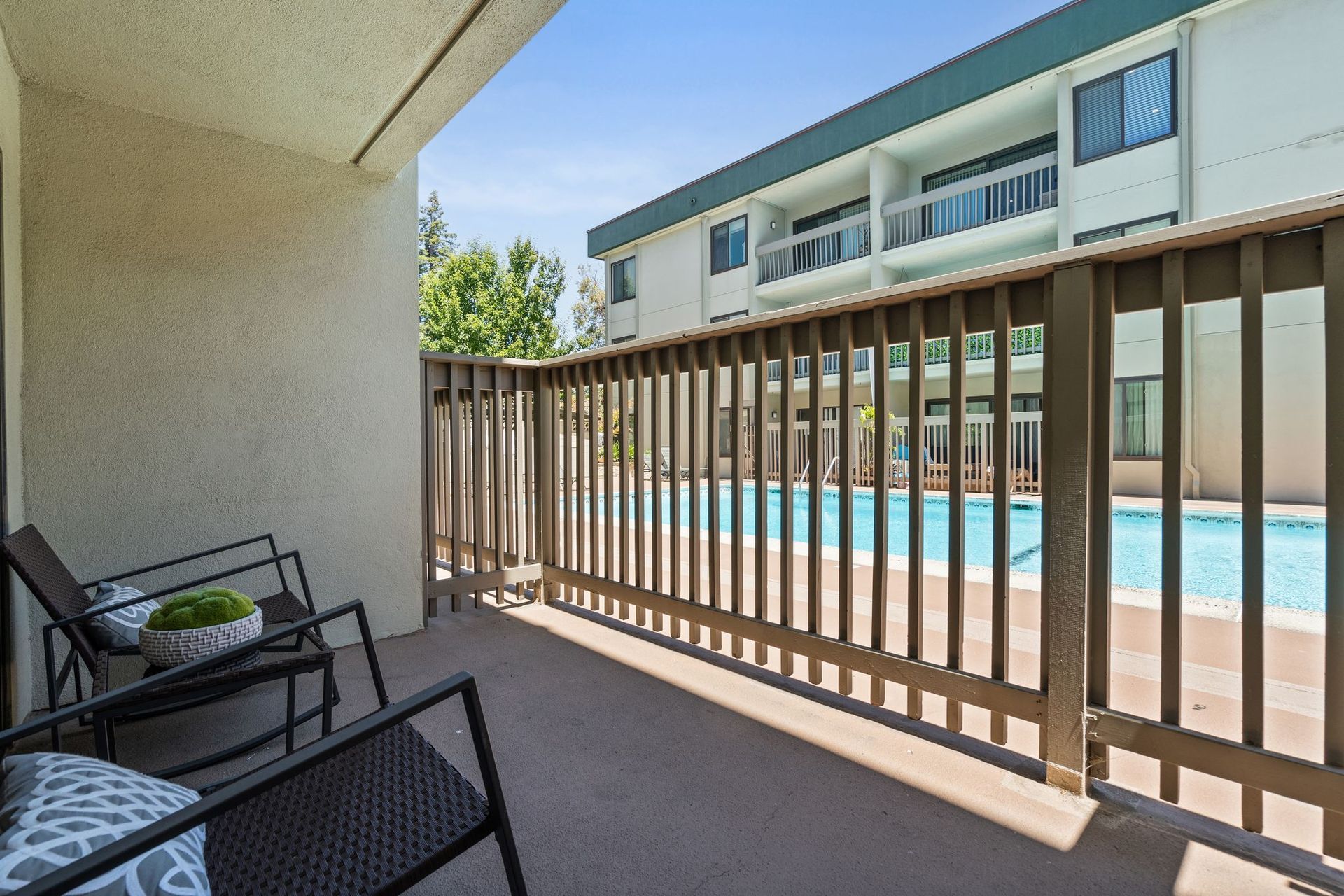 A balcony with chairs and a table overlooking a swimming pool.