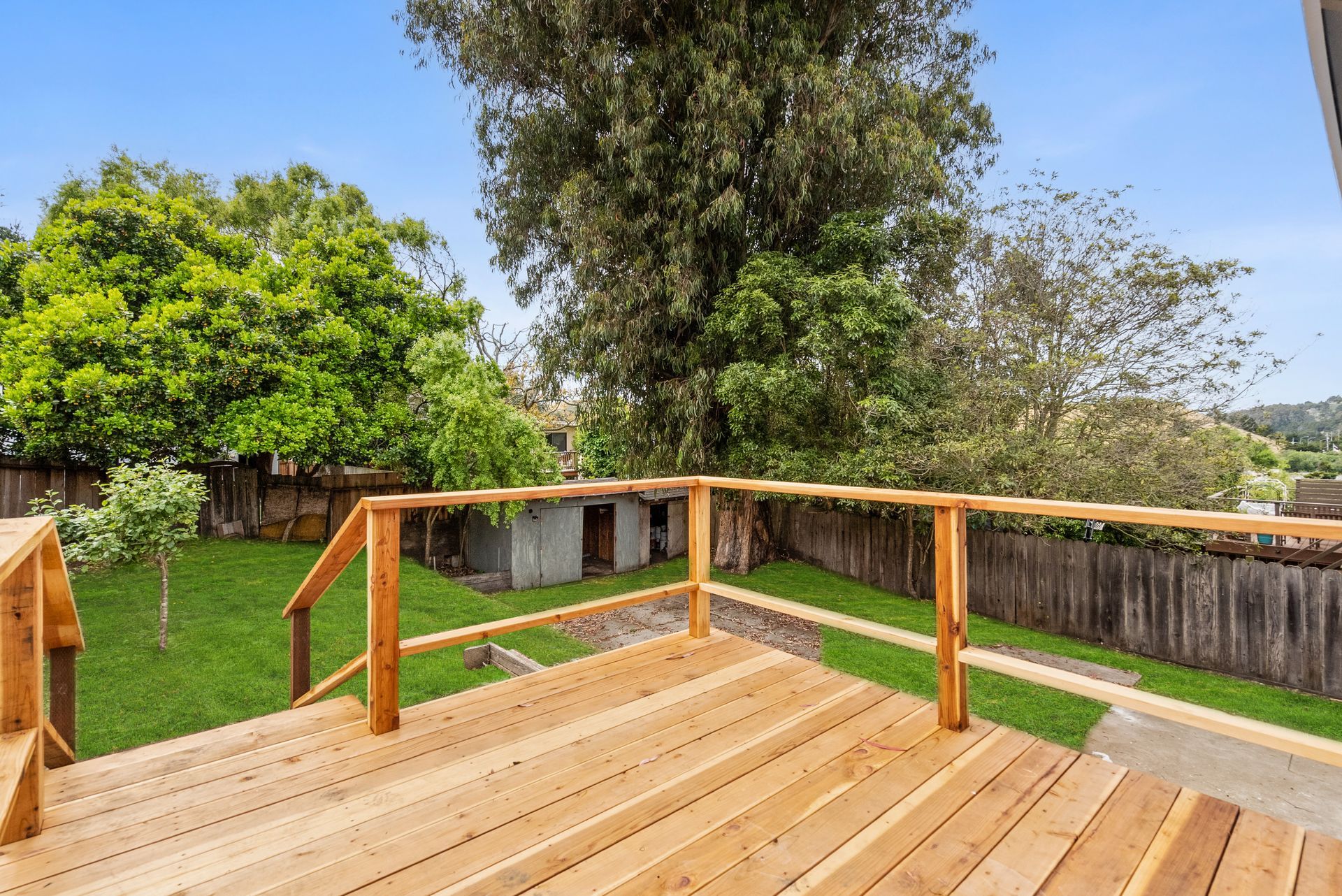 A wooden deck with a wooden railing overlooking a lush green yard.