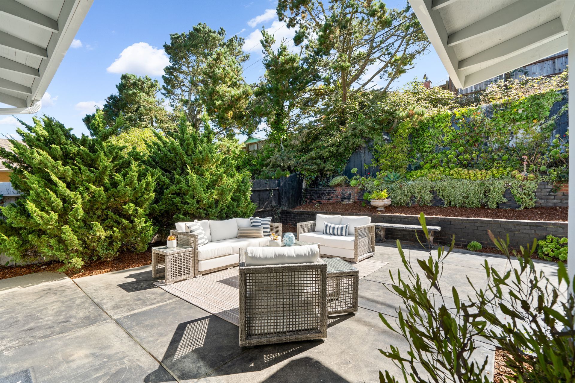 A patio with a couch , chairs , and a table surrounded by trees.