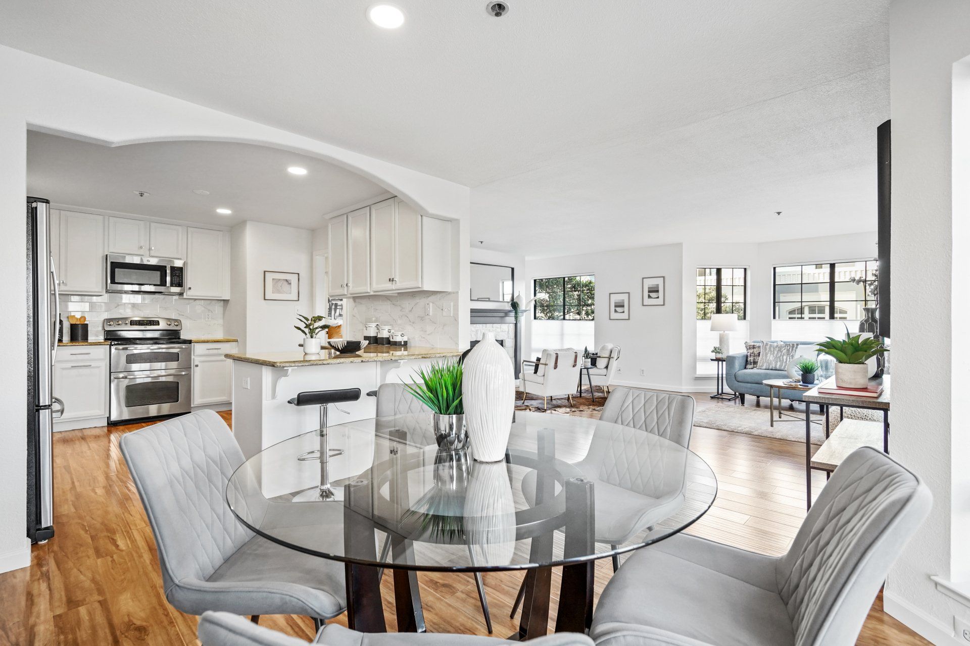 A dining room with a glass table and chairs and a kitchen in the background.
