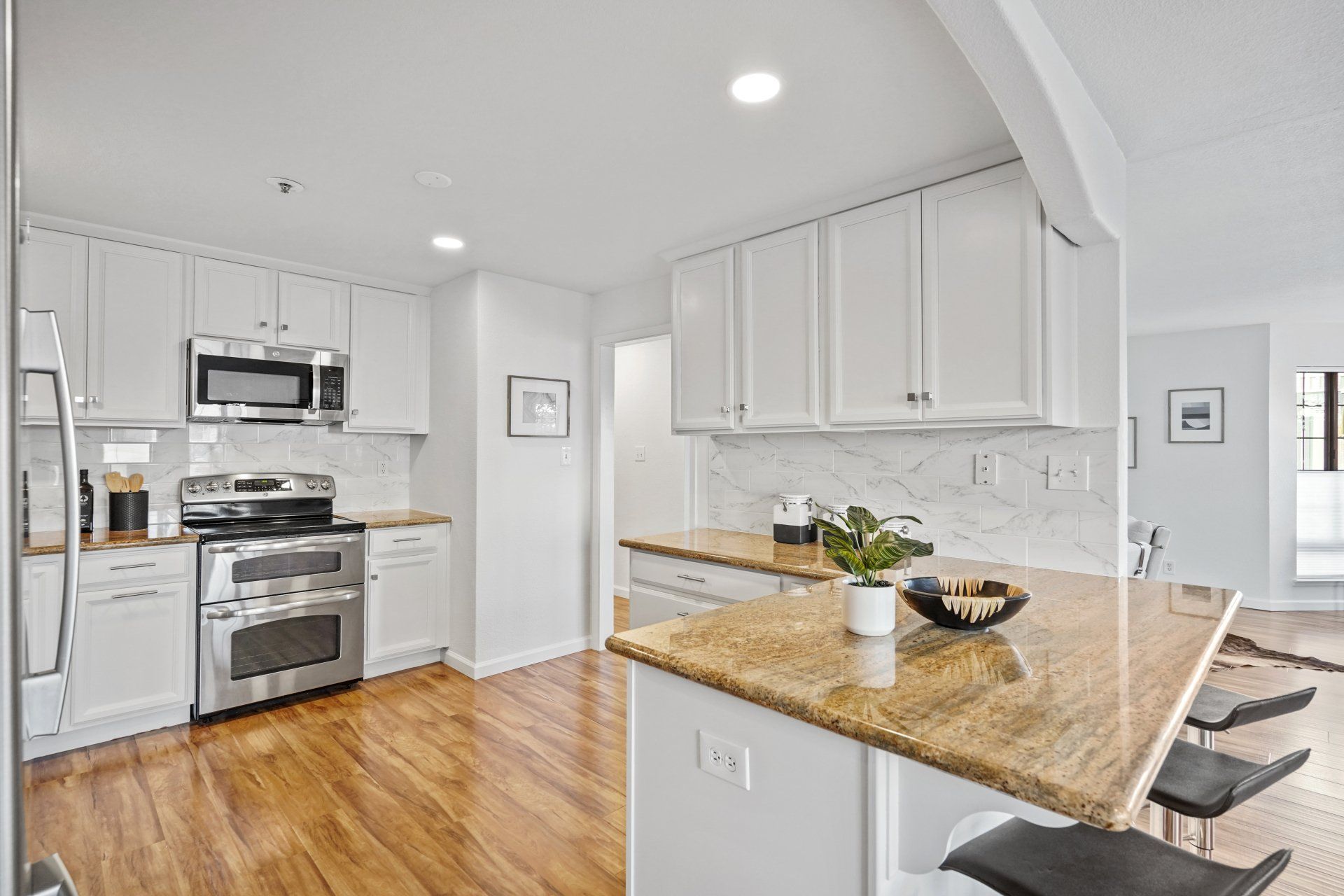 A kitchen with white cabinets , granite counter tops , stainless steel appliances and hardwood floors.