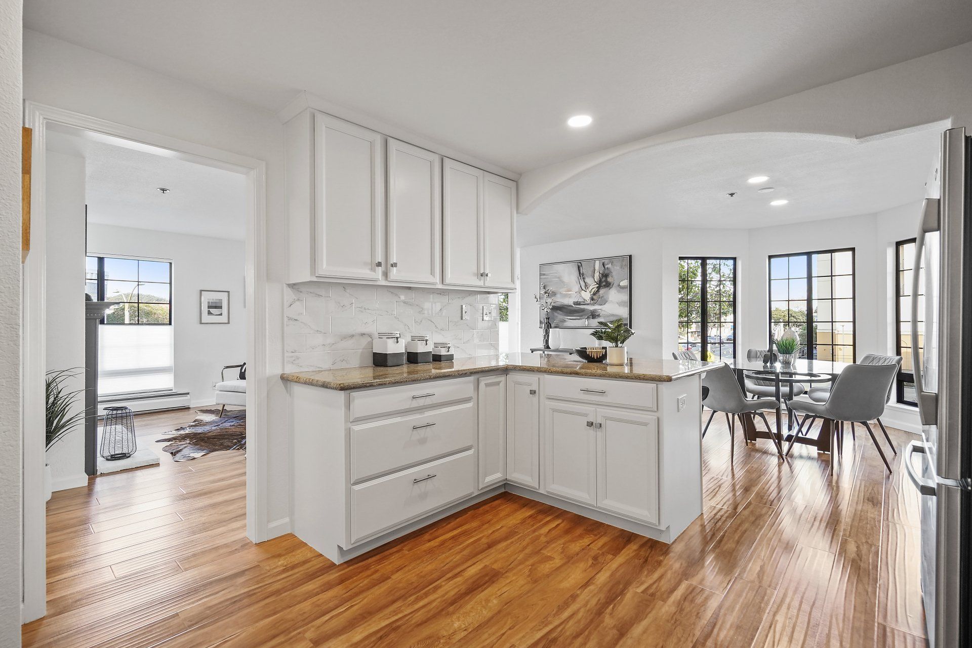 A kitchen with white cabinets , hardwood floors , and a refrigerator.