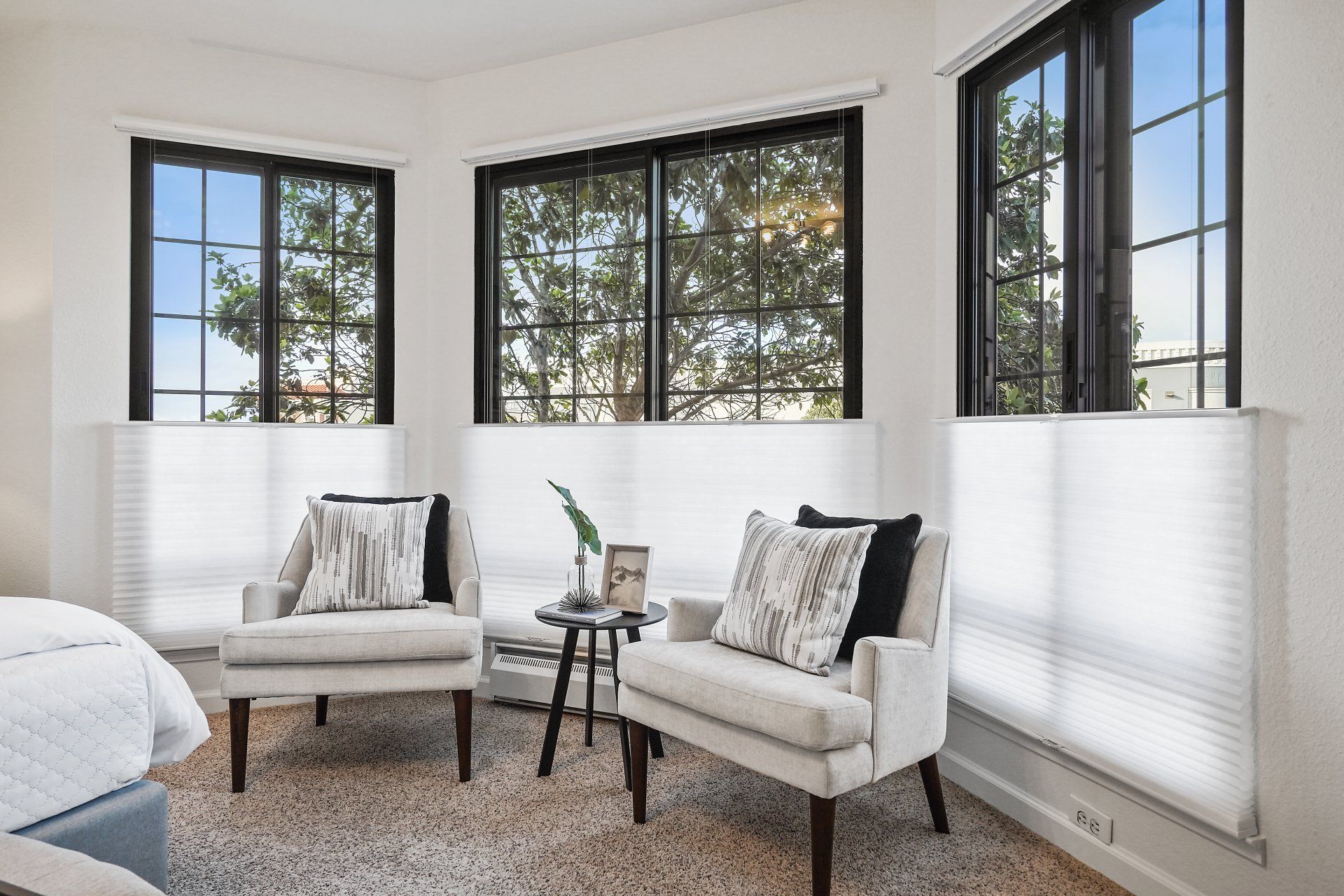 A bedroom with two chairs and a table in front of a bed.