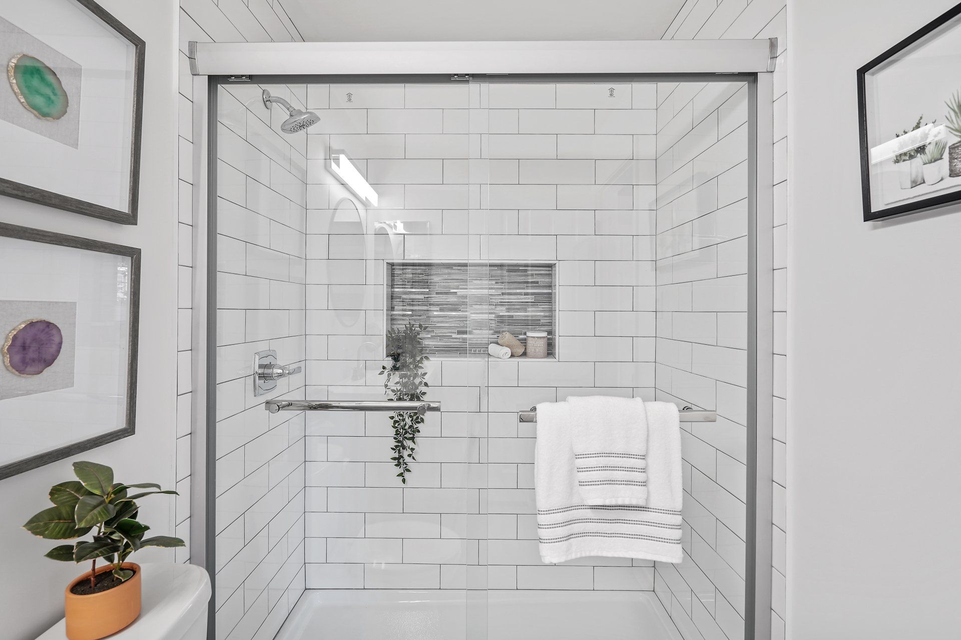 A bathroom with white tiles and a sliding glass shower door.