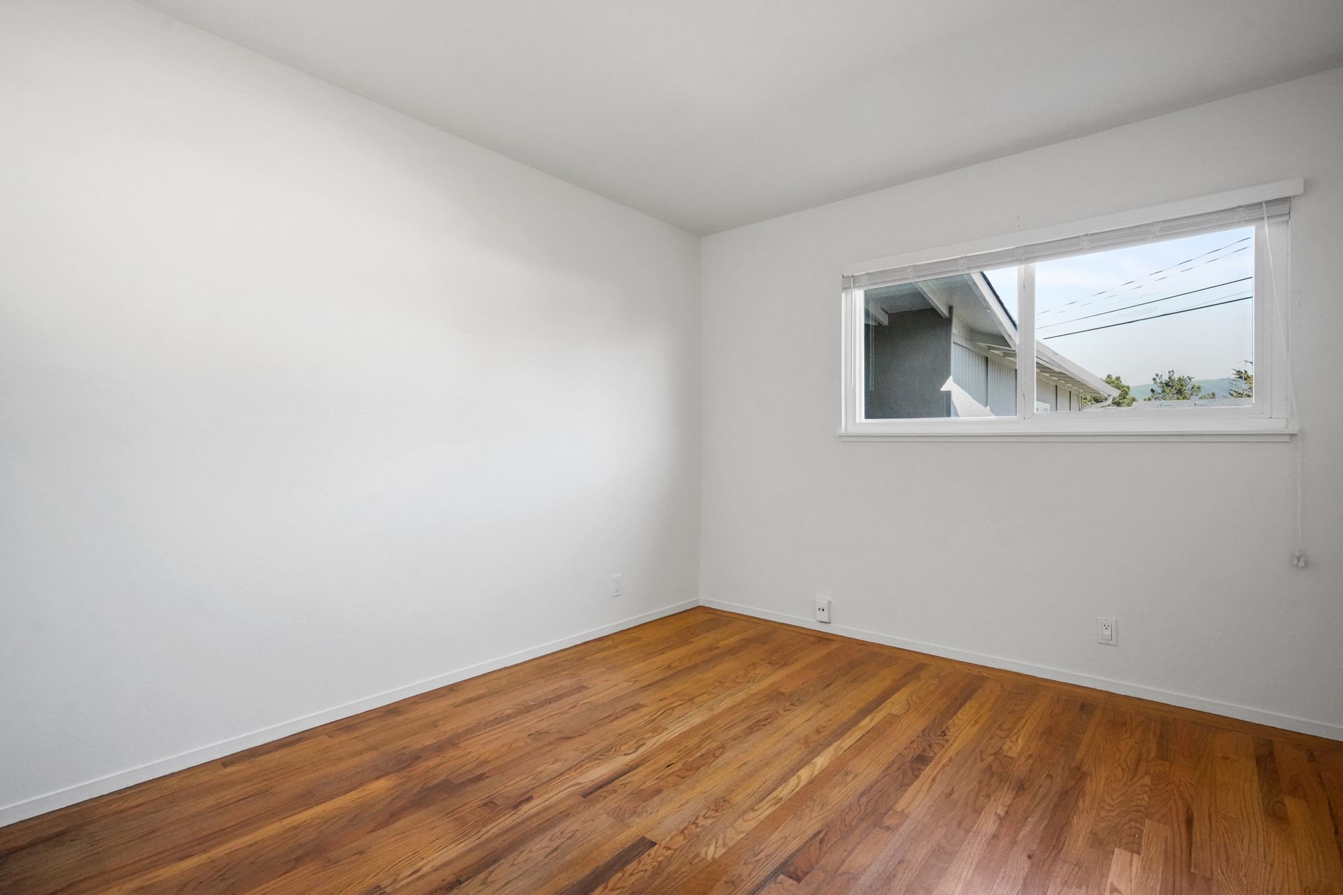 An empty room with hardwood floors and a window.