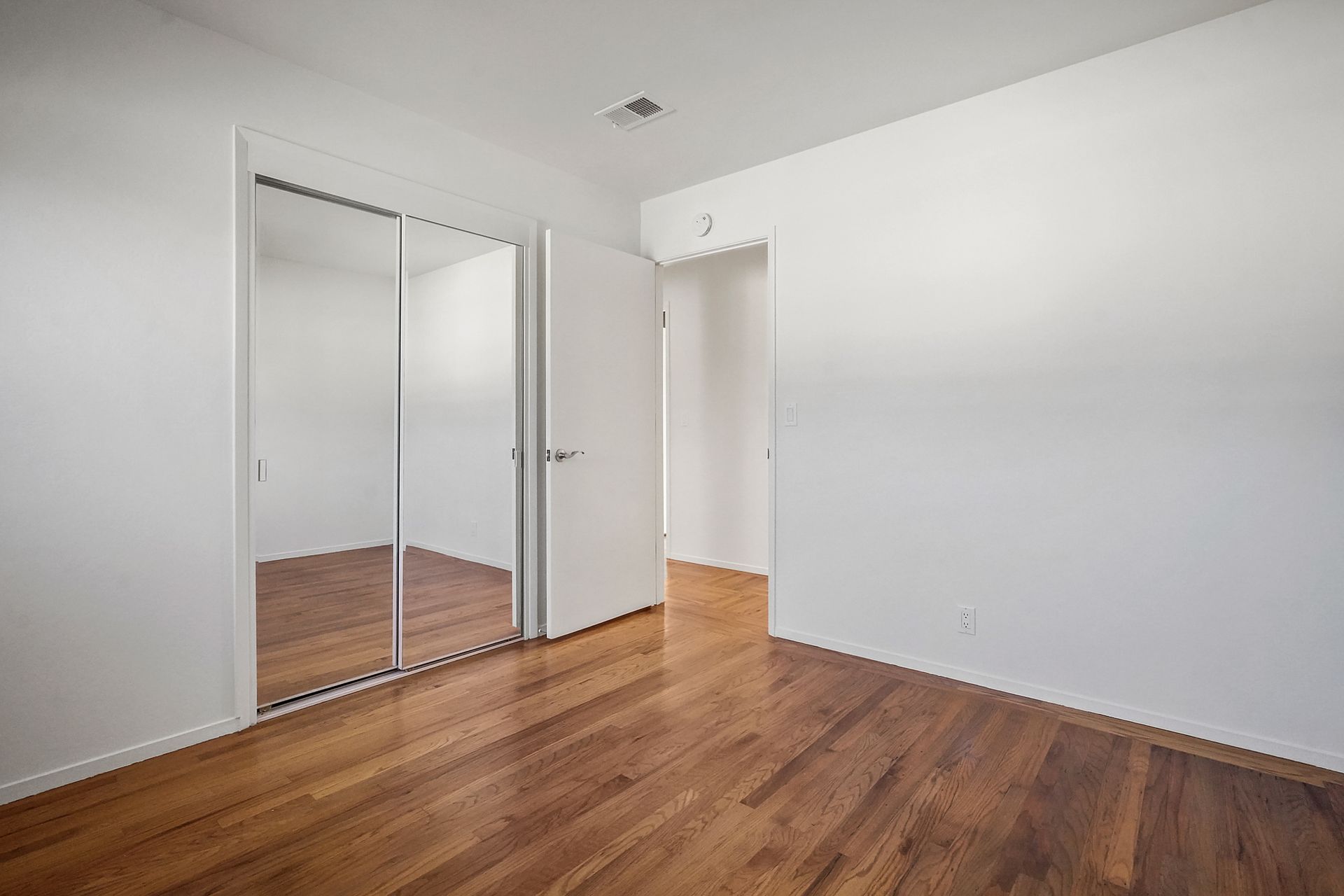 An empty bedroom with hardwood floors and sliding glass doors.
