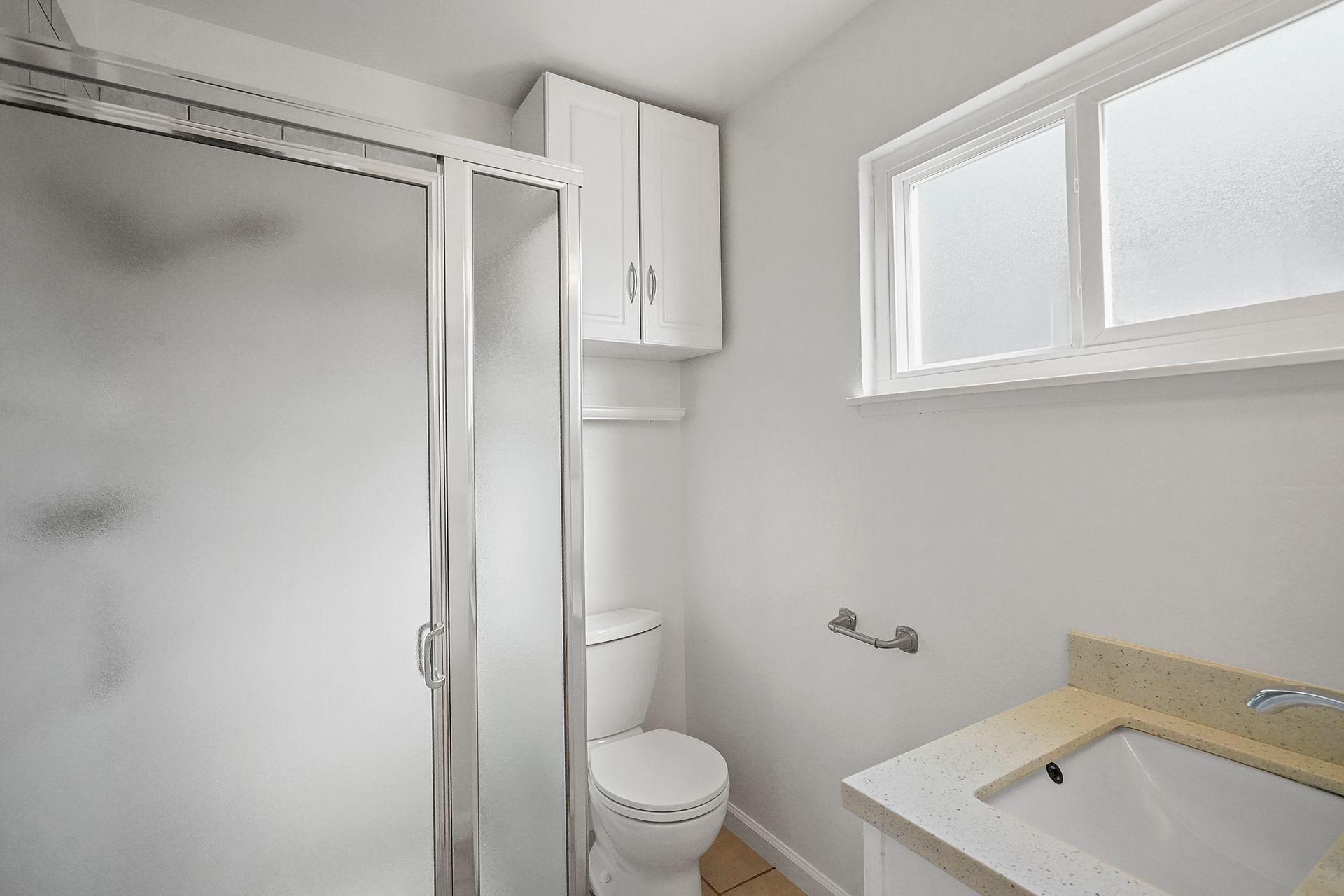 A bathroom with a toilet , sink , shower and window.