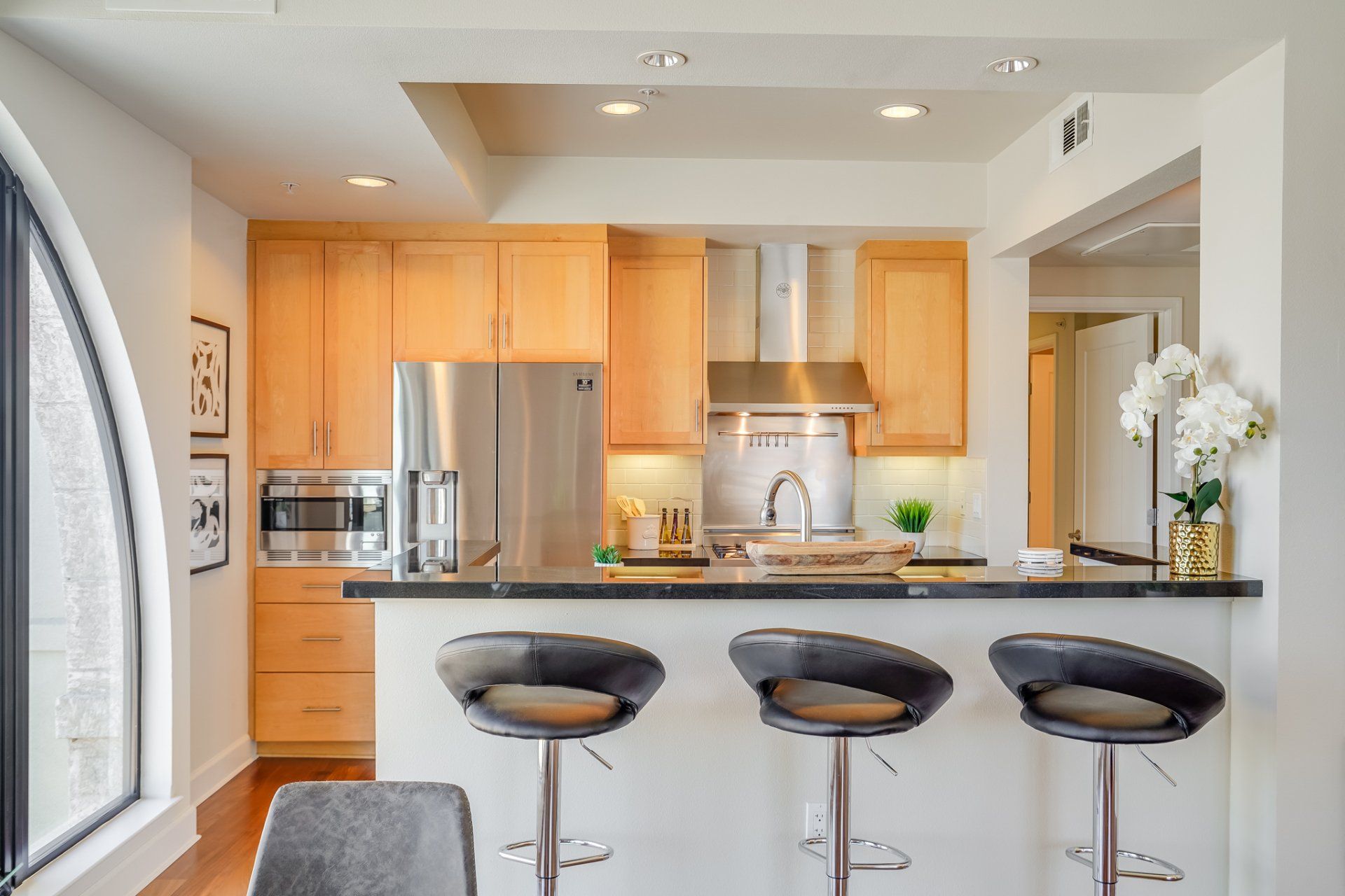 A kitchen with three bar stools and a stainless steel refrigerator