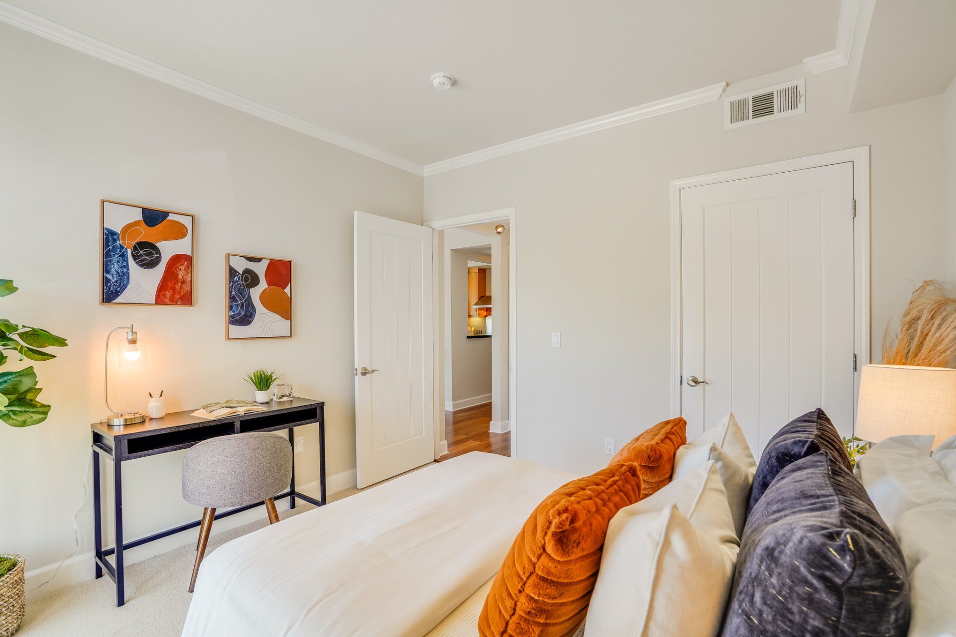 A bedroom with a bed , desk , chair and paintings on the wall.