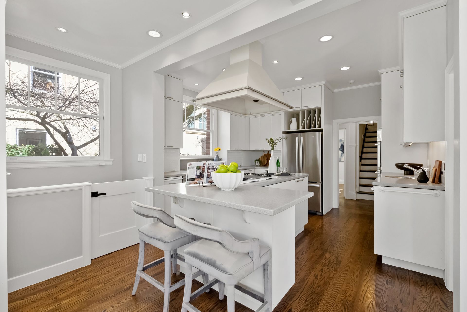 A kitchen with white cabinets , hardwood floors , stainless steel appliances and a large island.