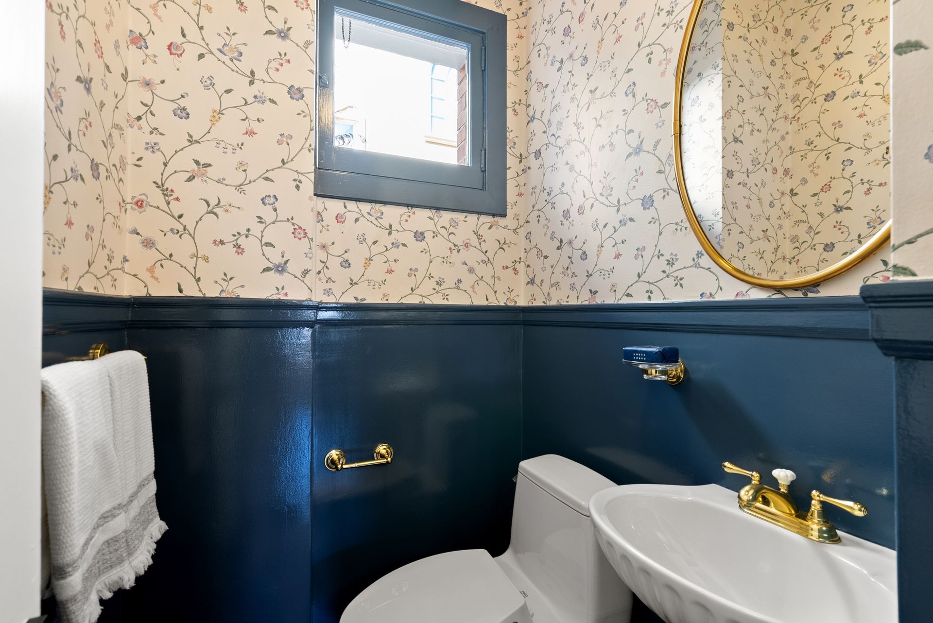 A bathroom with a toilet , sink , mirror and window.