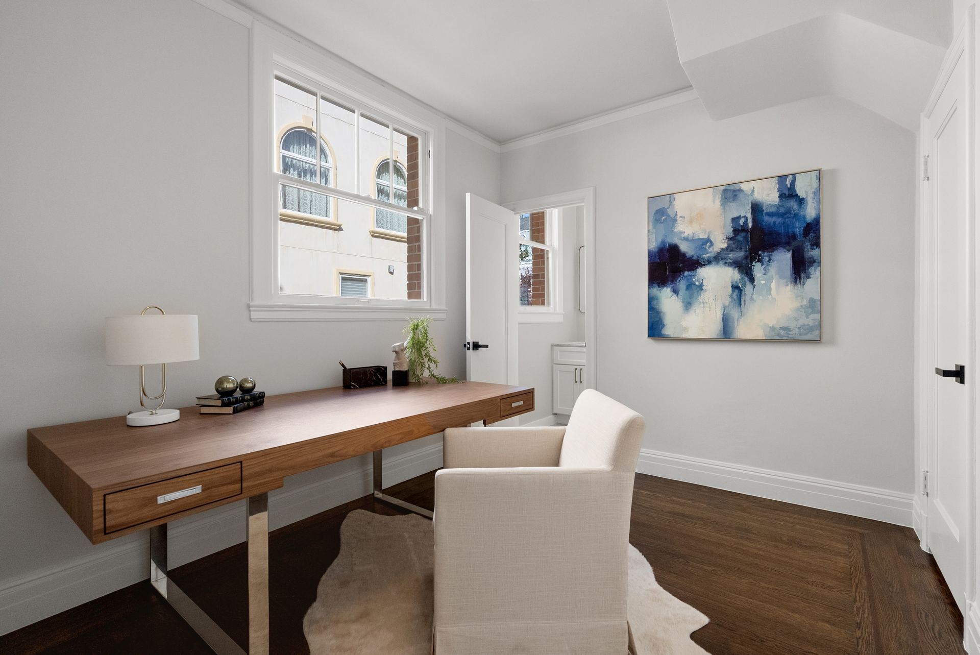 A room with a desk and chair and a painting on the wall