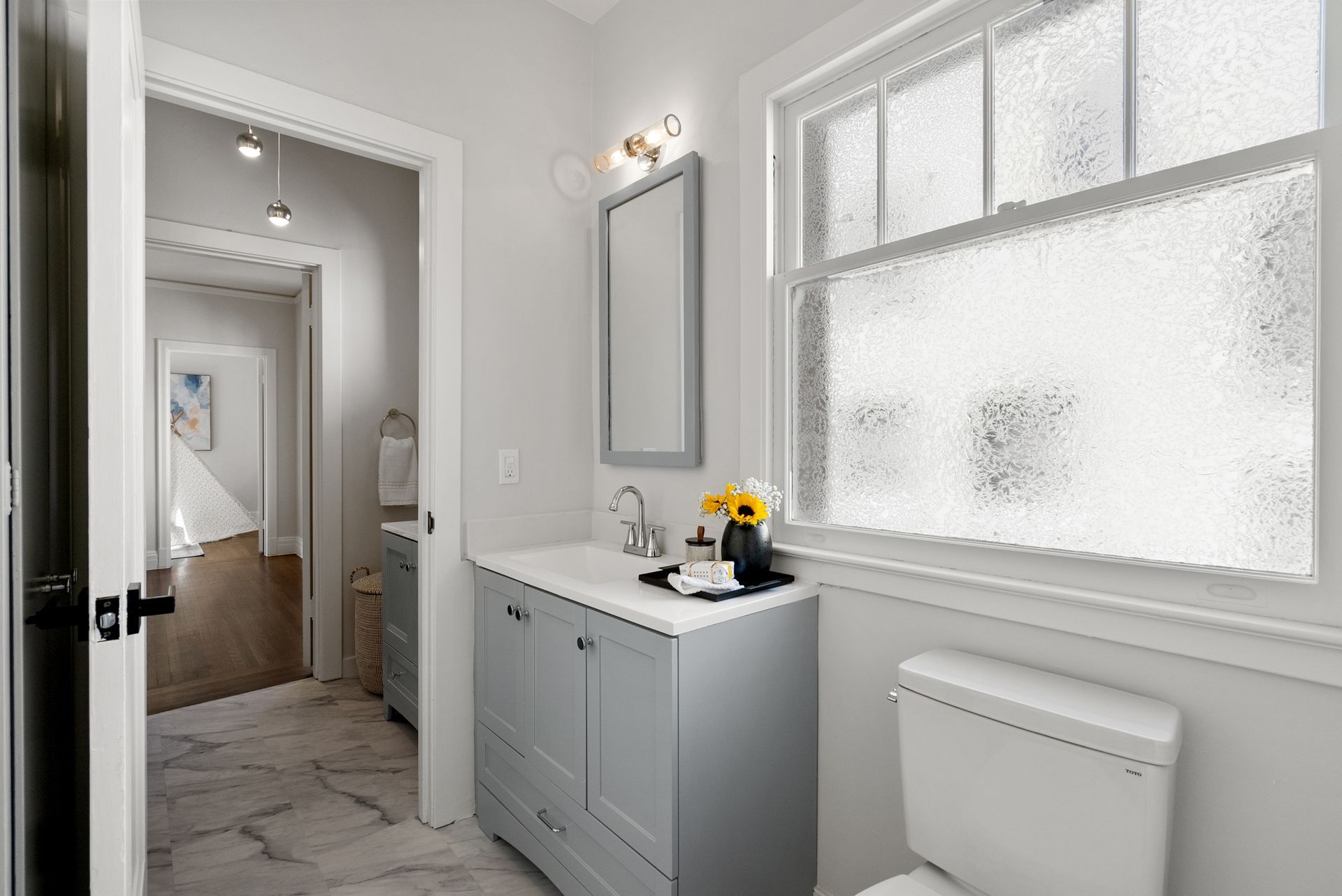 A bathroom with a toilet , sink , mirror and window.