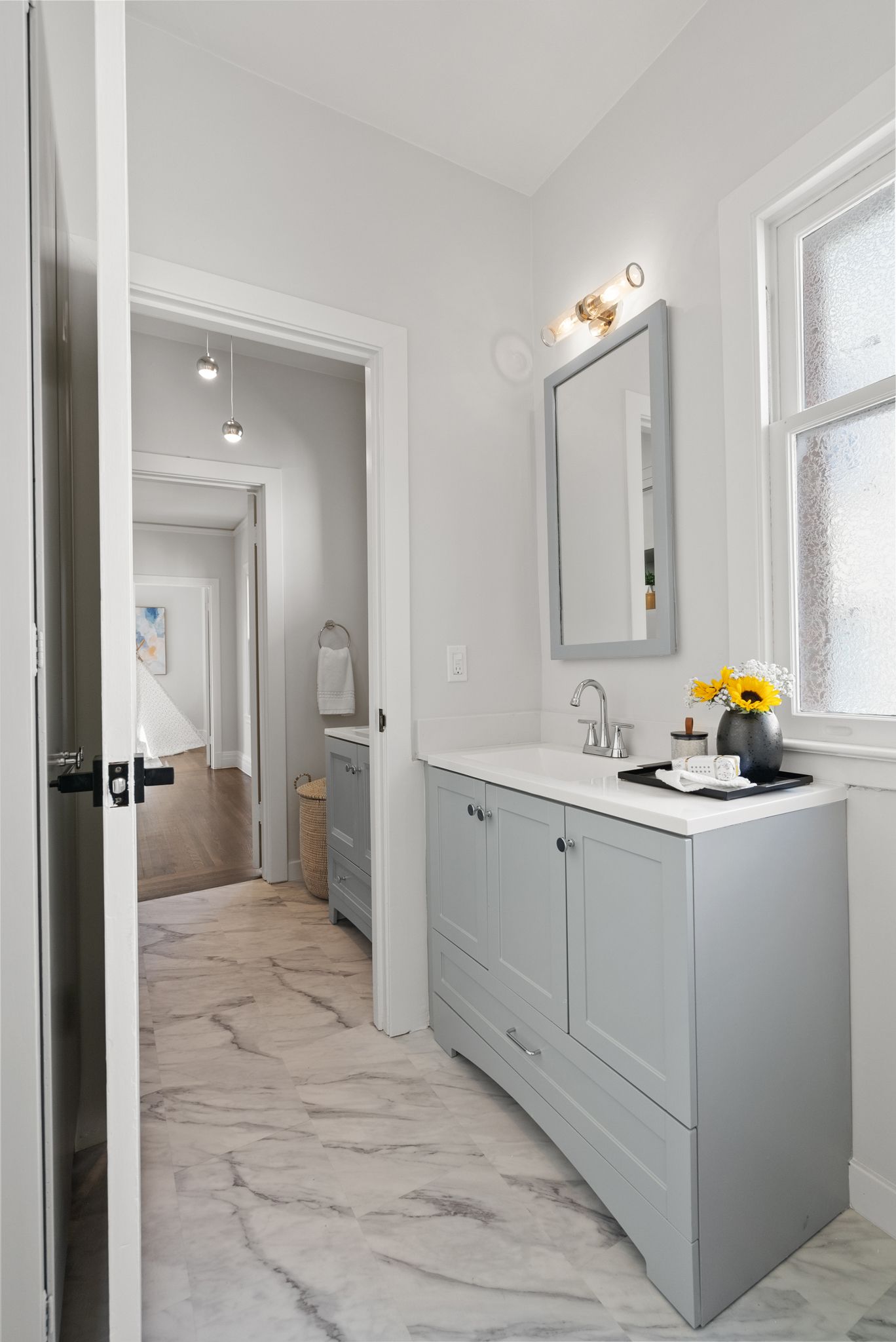 A bathroom with a sink , mirror , and a vase with flowers.