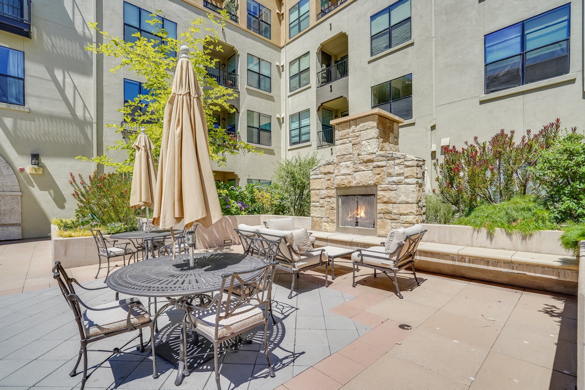 A patio with a table and chairs and umbrellas in front of a building with a fireplace.