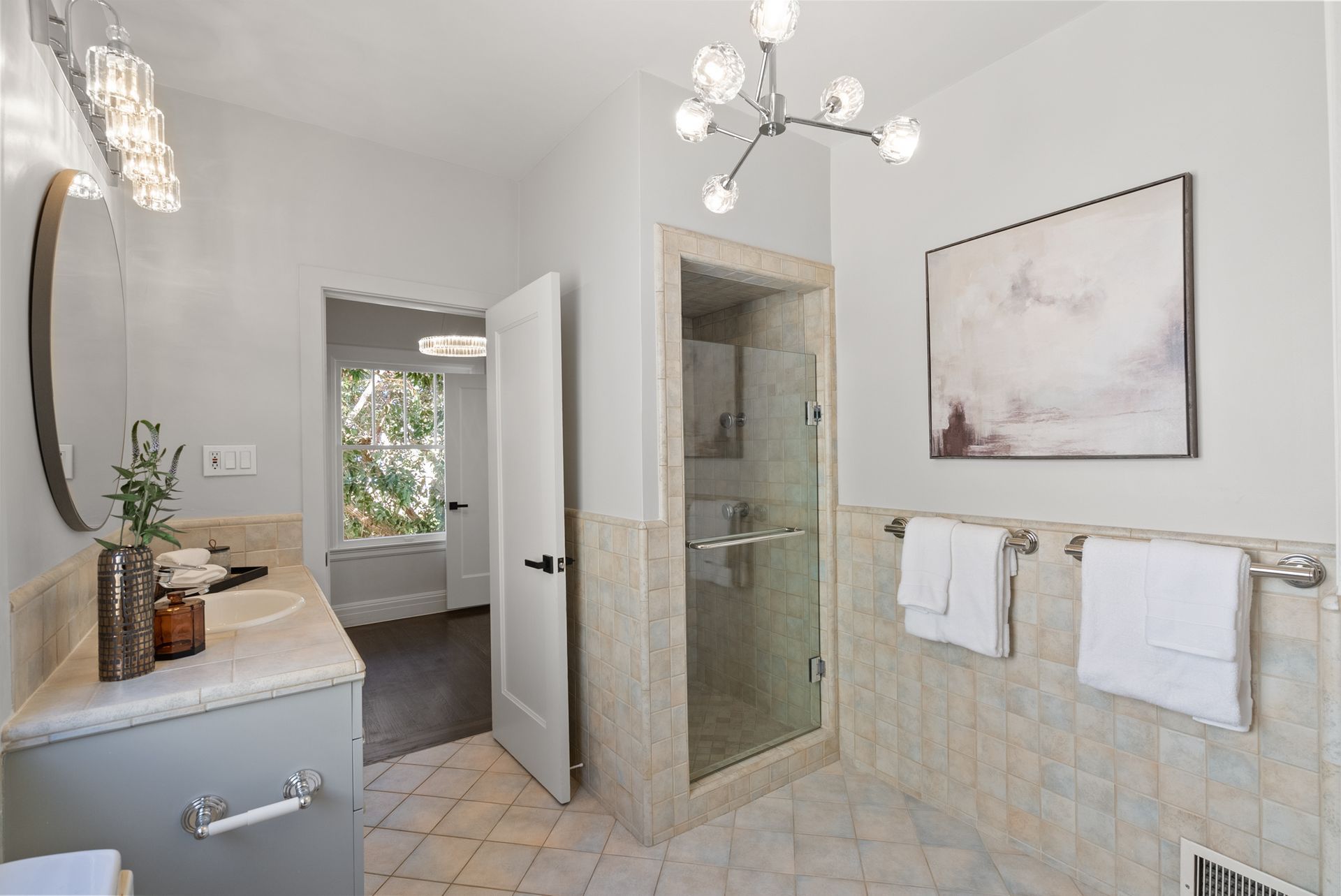 A bathroom with a walk in shower , sink , mirror and painting on the wall.