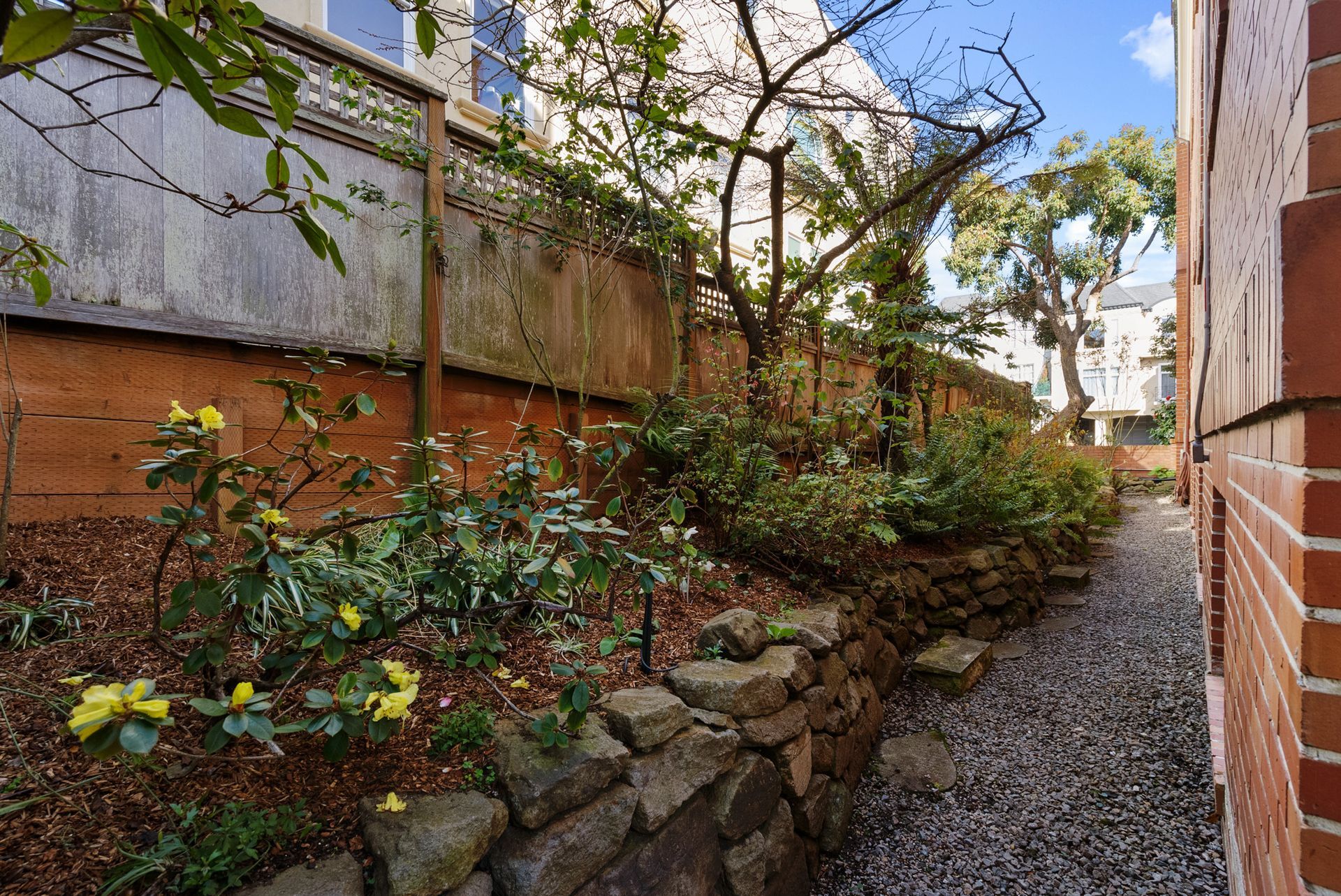 A stone wall surrounds a garden next to a brick building.