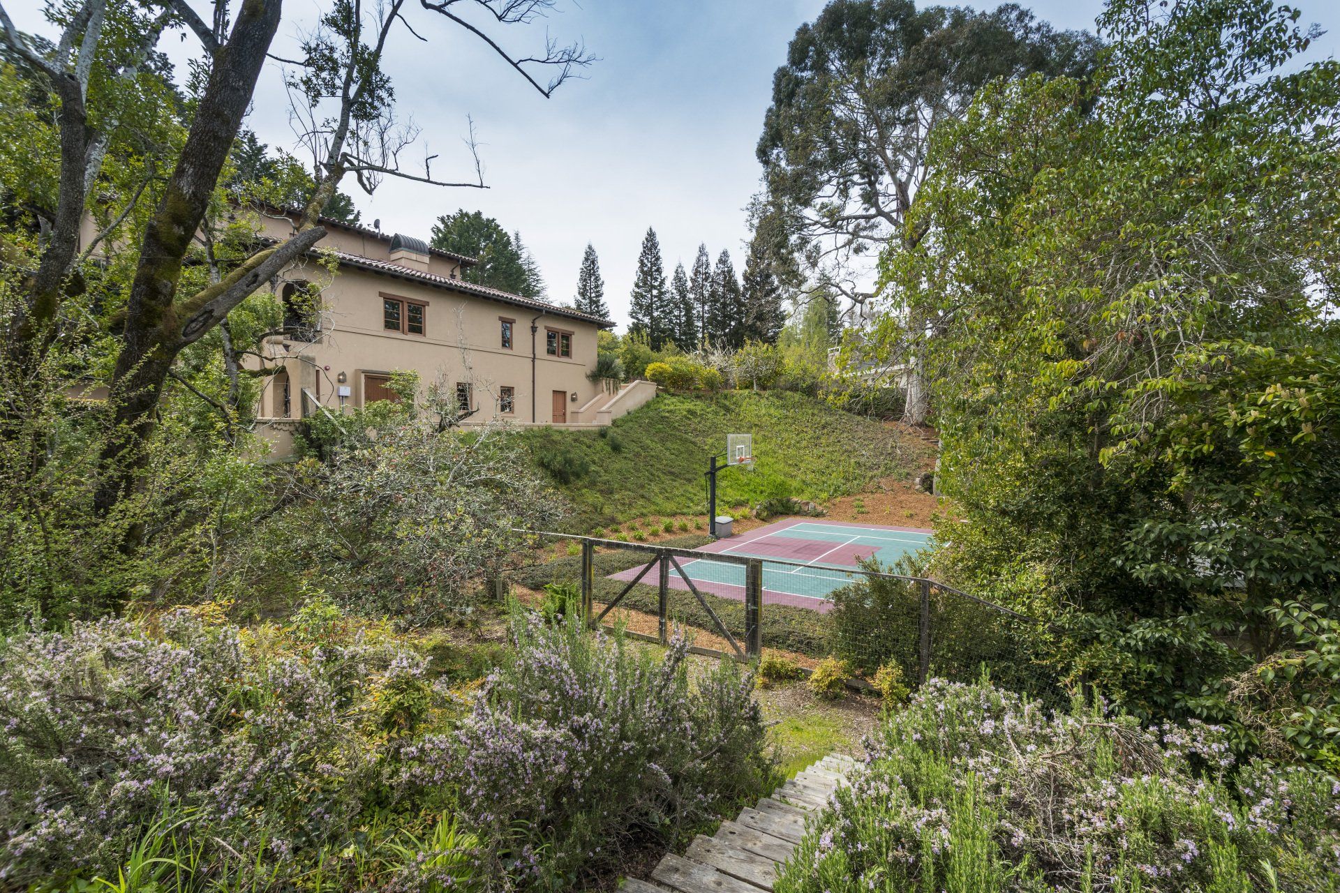A large house is surrounded by trees and a tennis court.