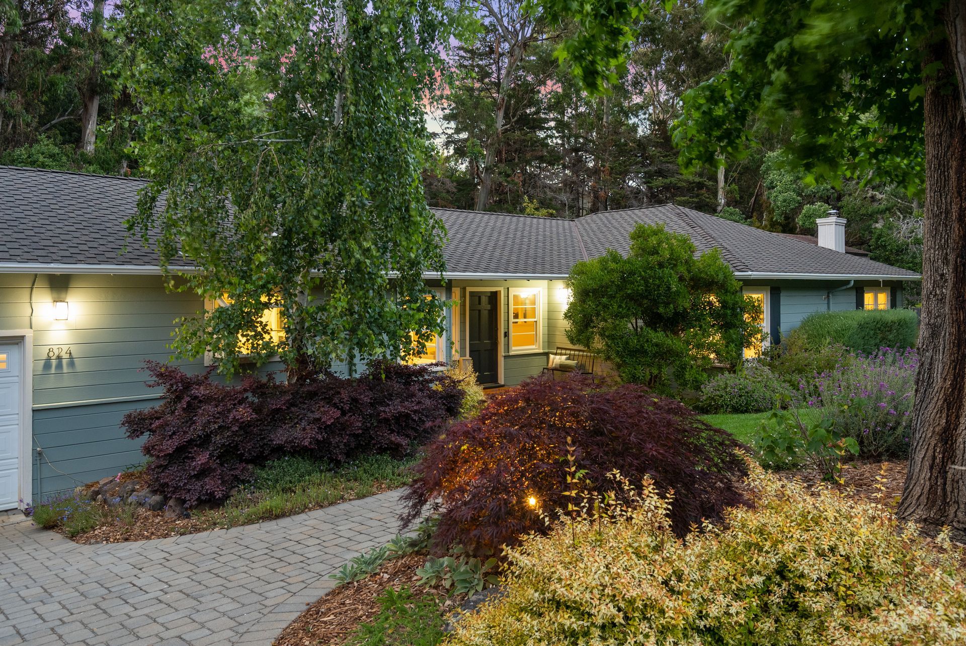 A house with a brick driveway and a tree in front of it.