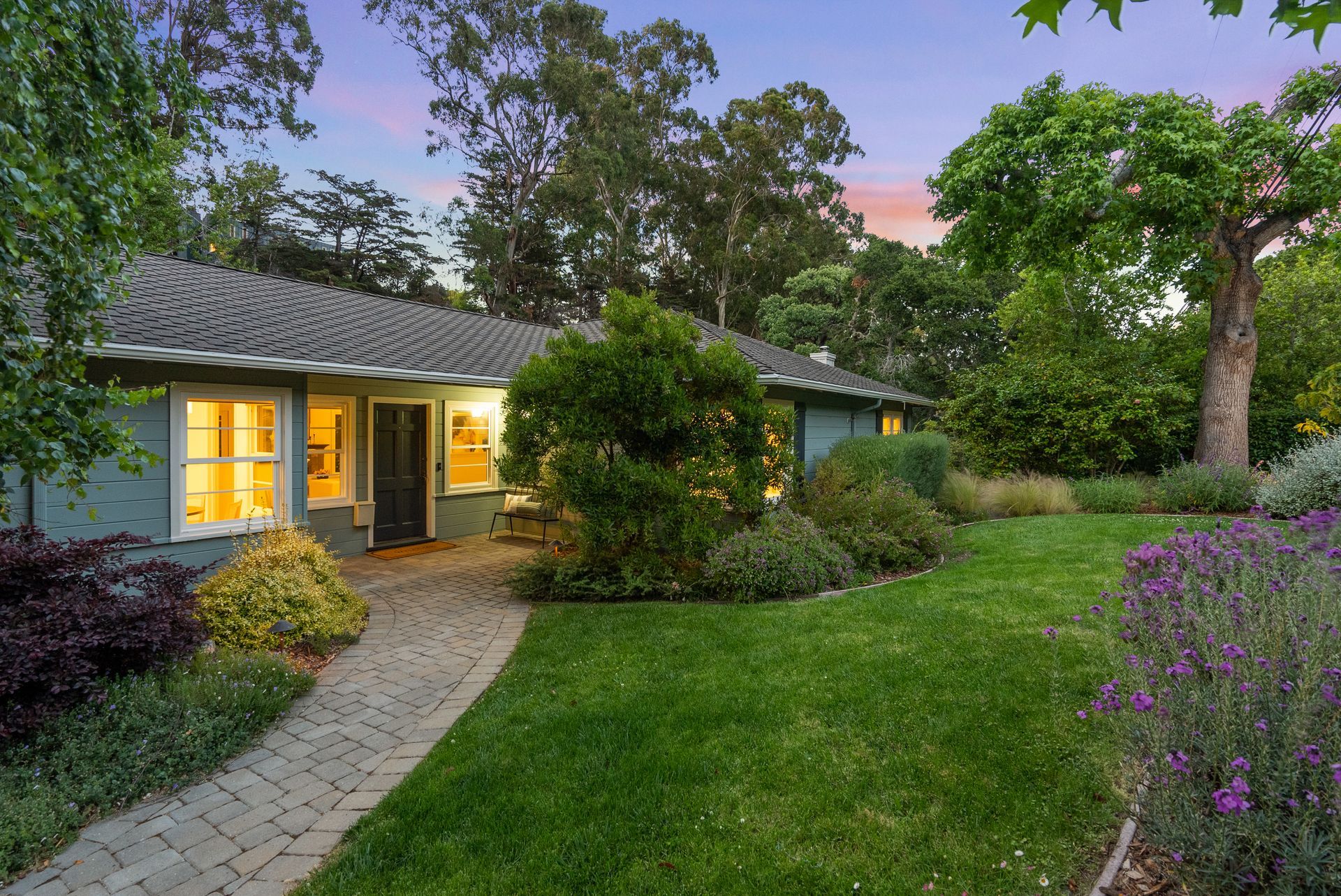 A house with a lush green lawn and a brick walkway leading to it.
