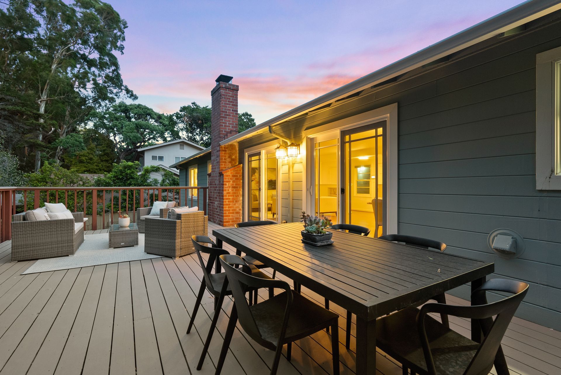 There is a large table and chairs on the deck of a house.