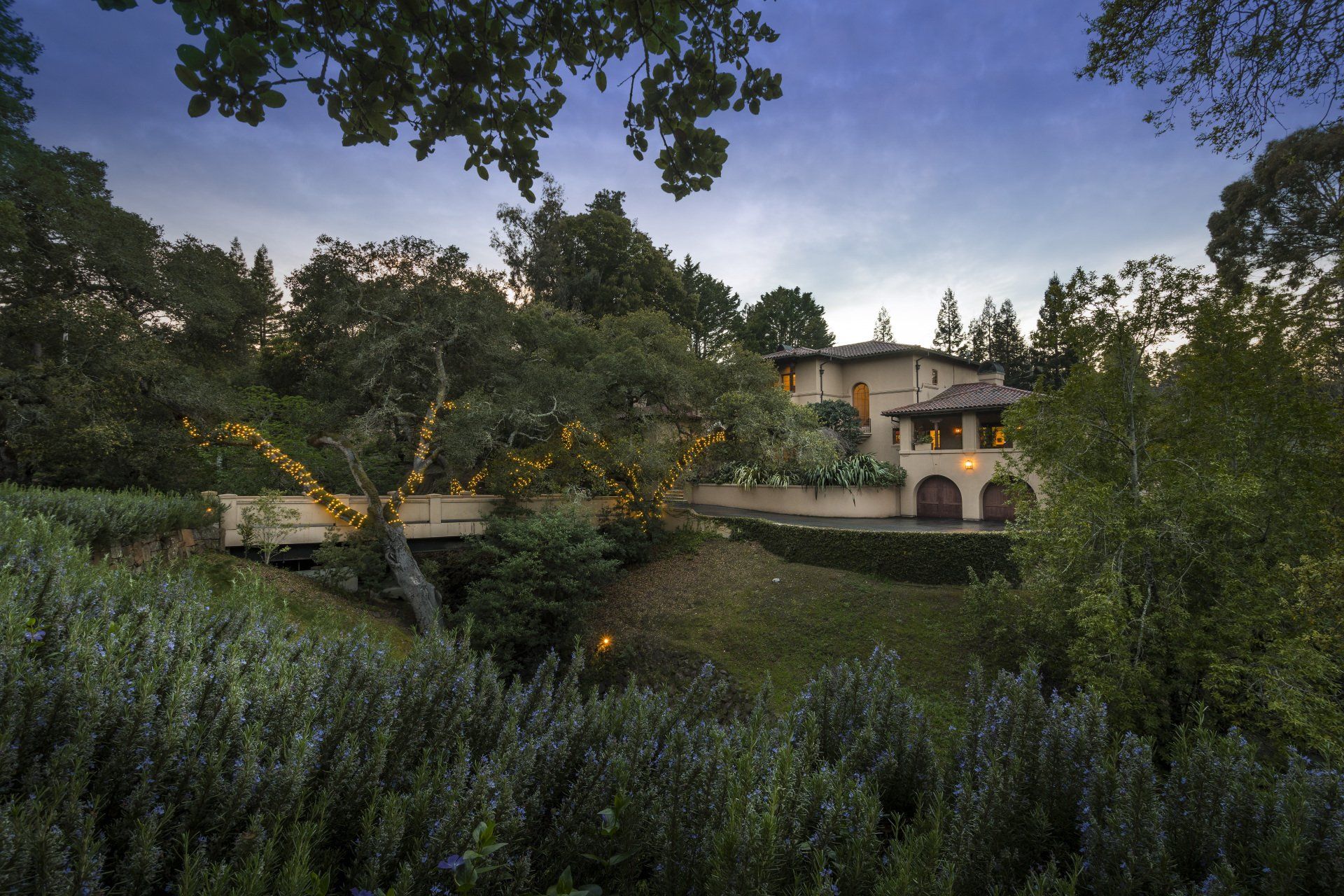 A large house is surrounded by trees and a bridge.