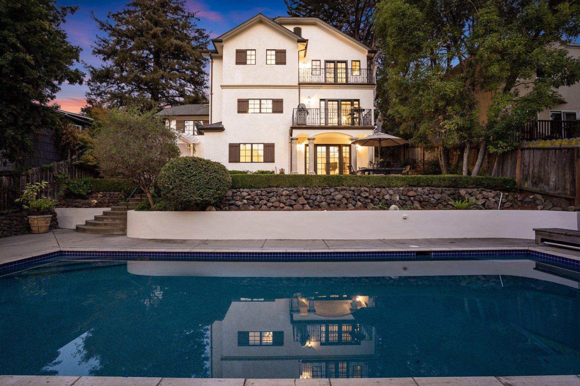 A white house with a pool, the house reflecting in the water at dusk.