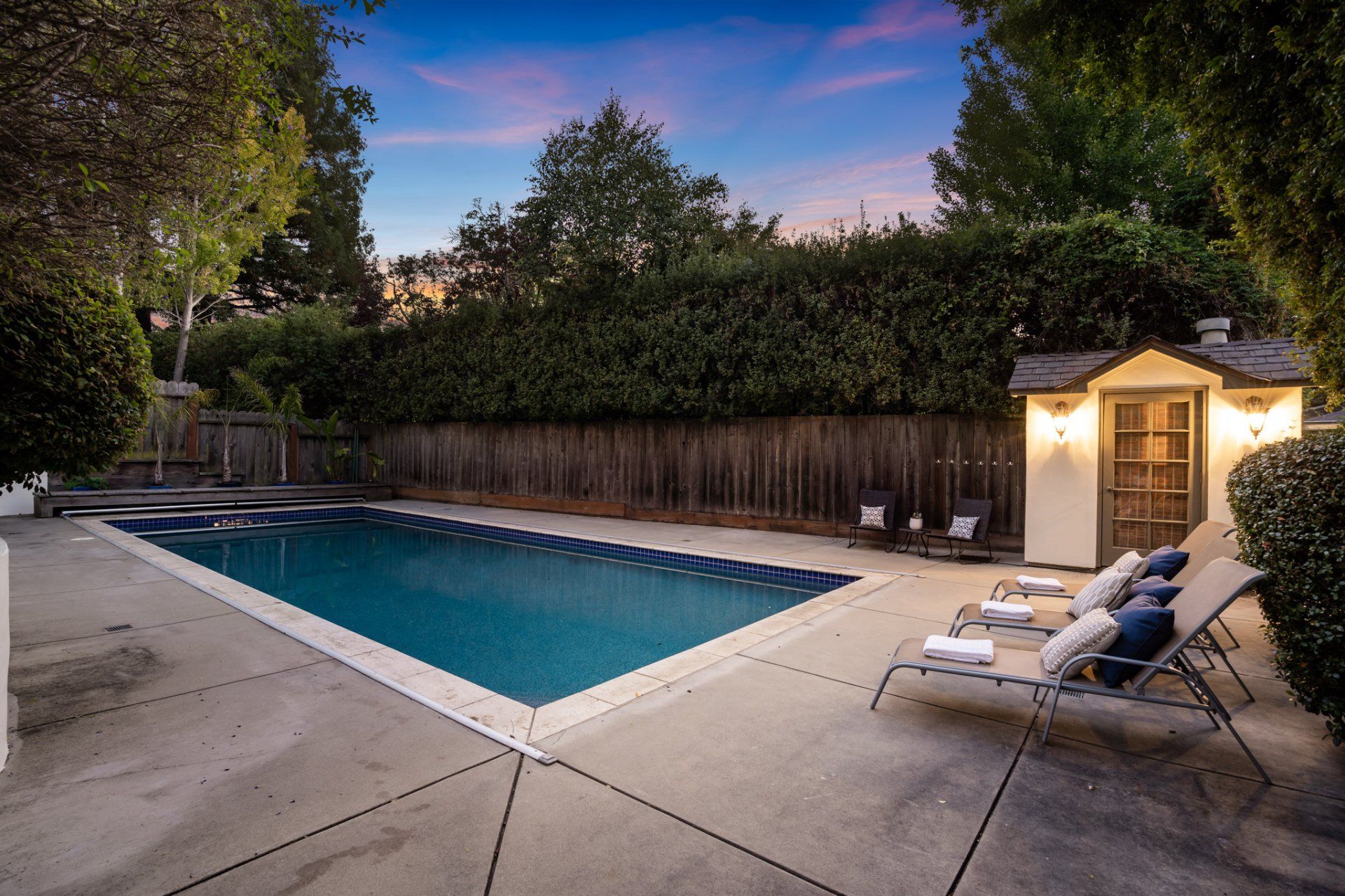 A large swimming pool is surrounded by chairs and a shed.
