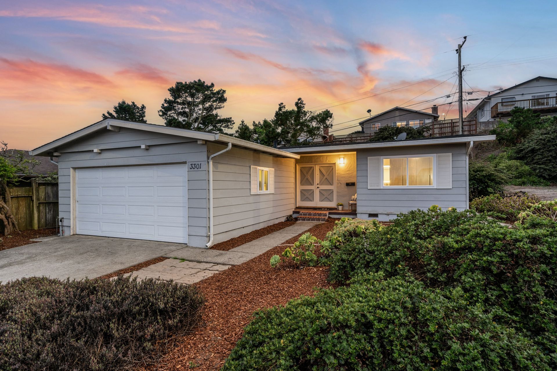 A white house with a garage and a sunset in the background