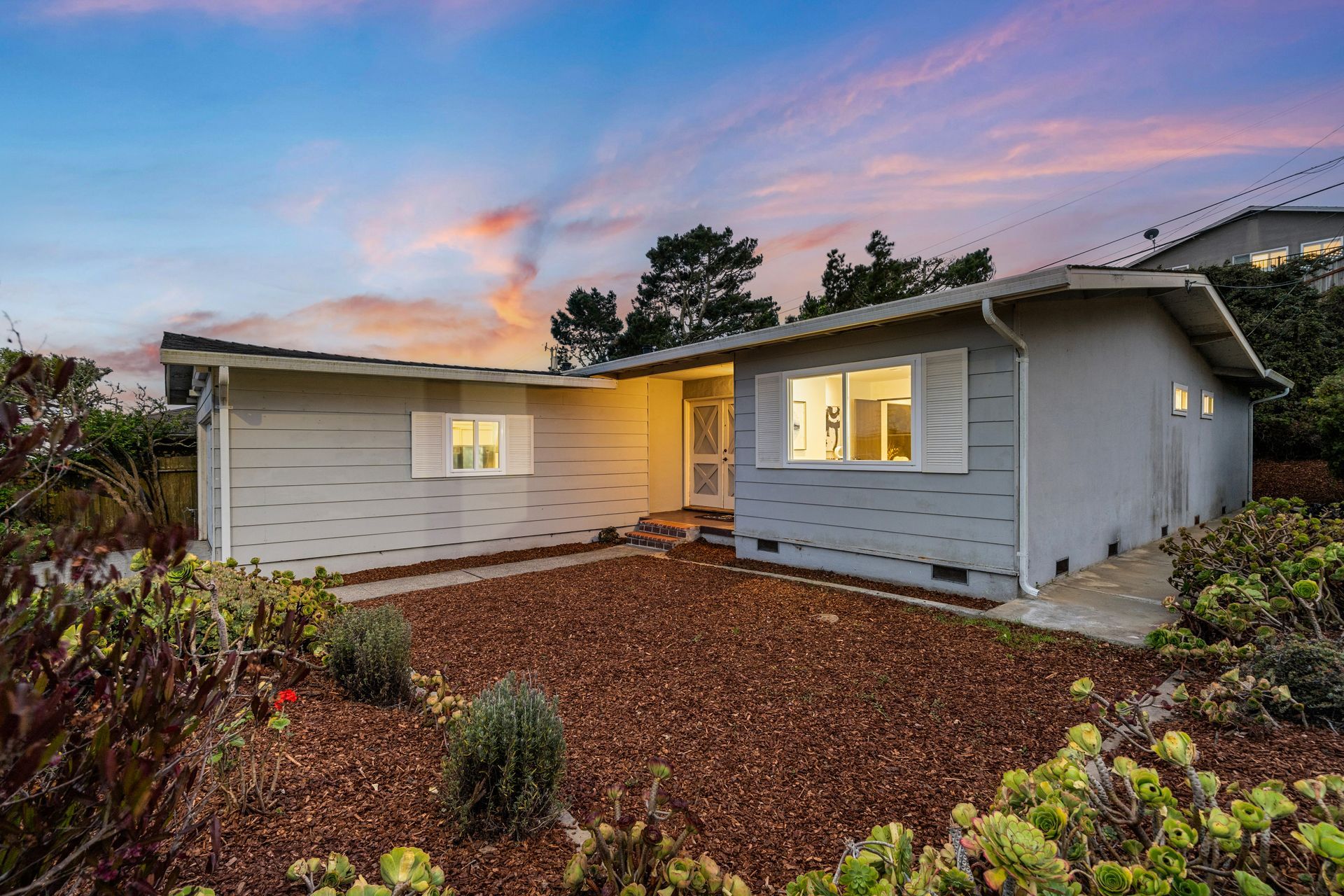 A house with light gray siding, a yard, and a dusk sky with pink and orange hues.
