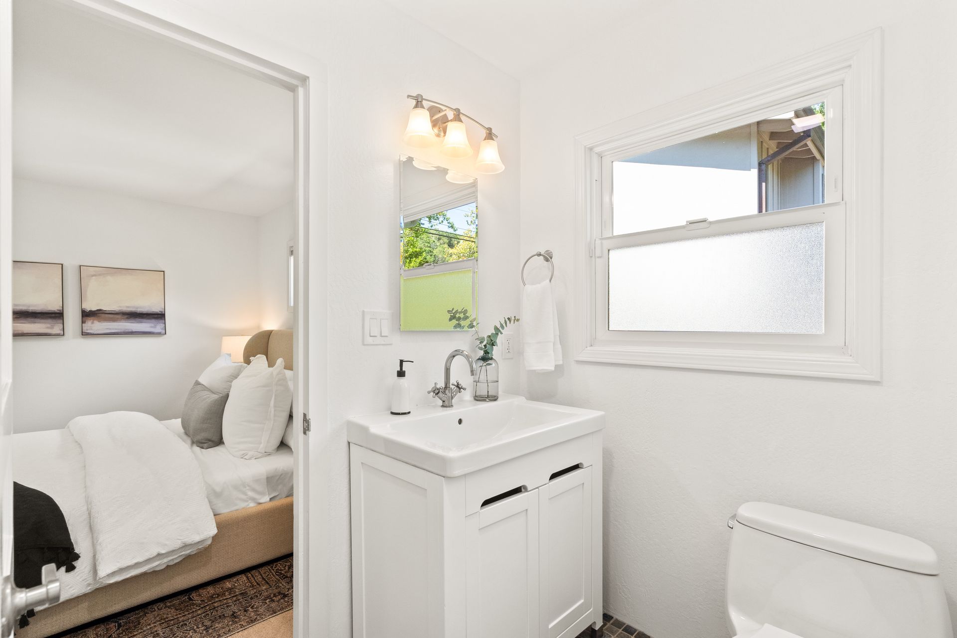A bathroom with a sink , toilet , mirror and window.