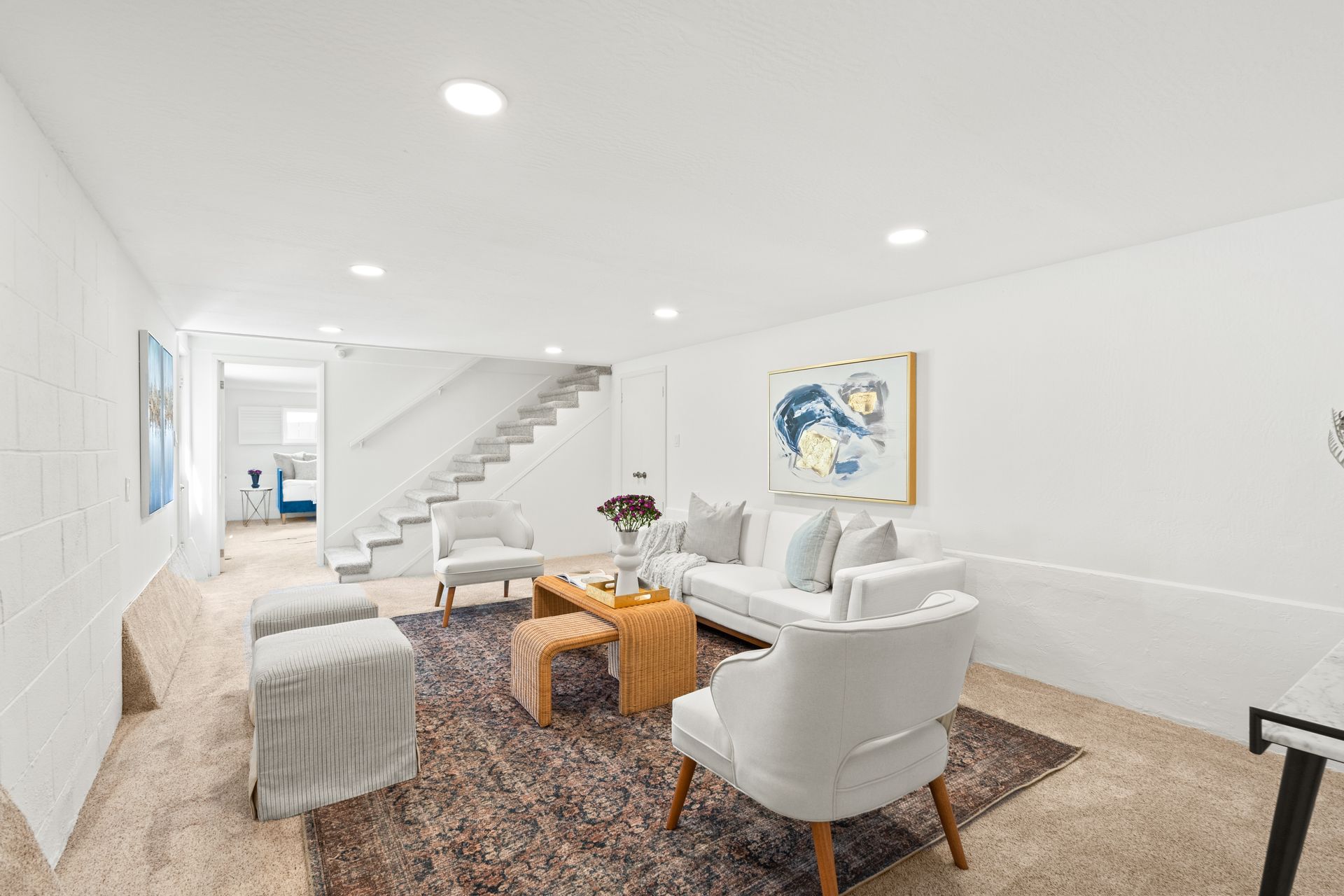 A room with a couch , chairs , coffee table and stairs.