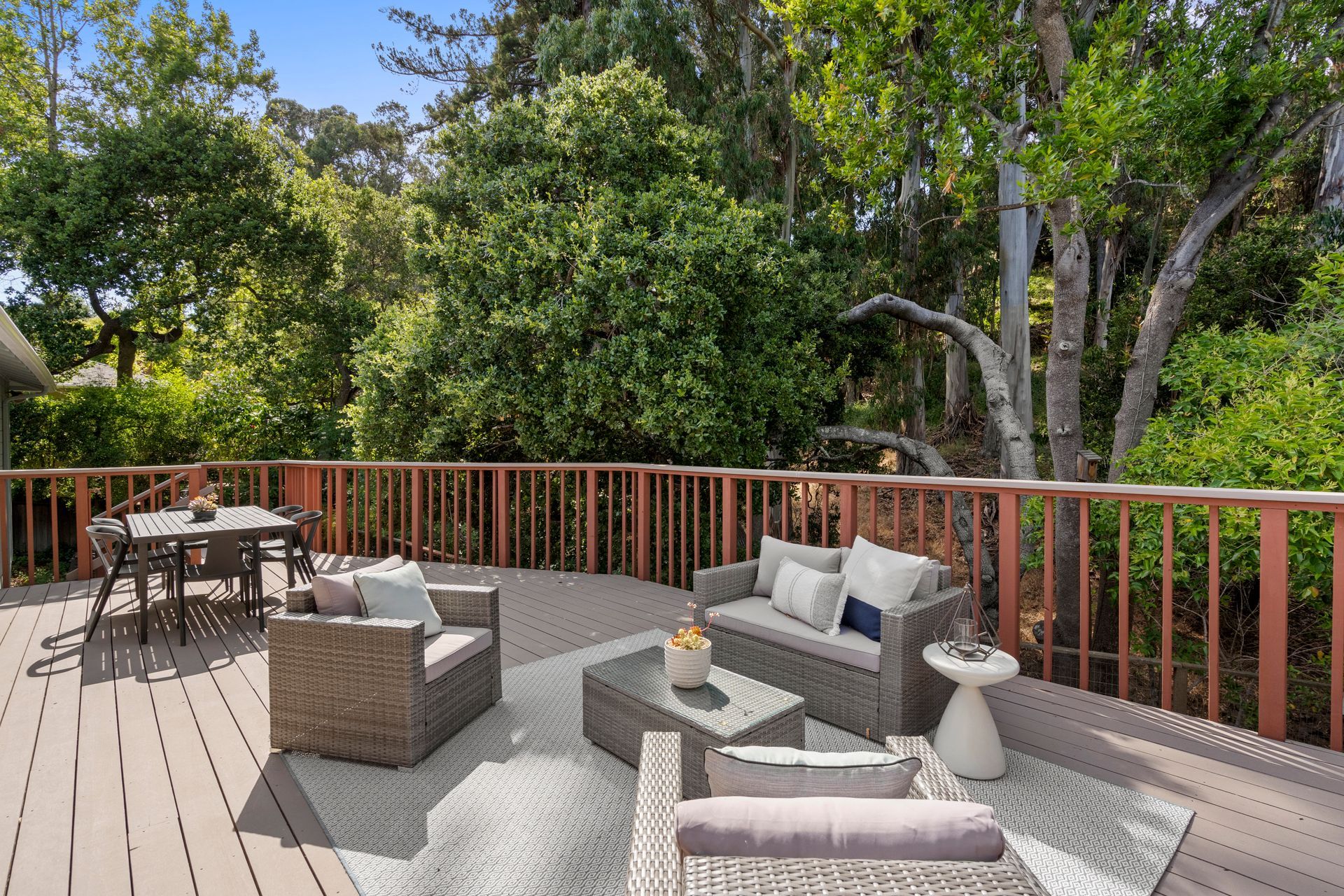A deck with a couch , chairs , table and rug surrounded by trees.