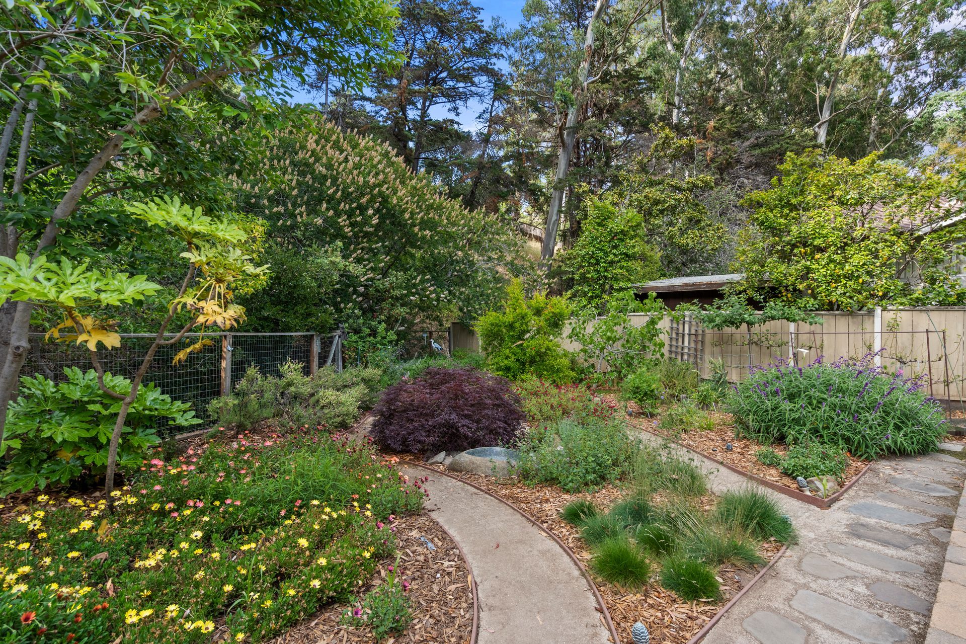 There is a path in the middle of the garden surrounded by trees and flowers.