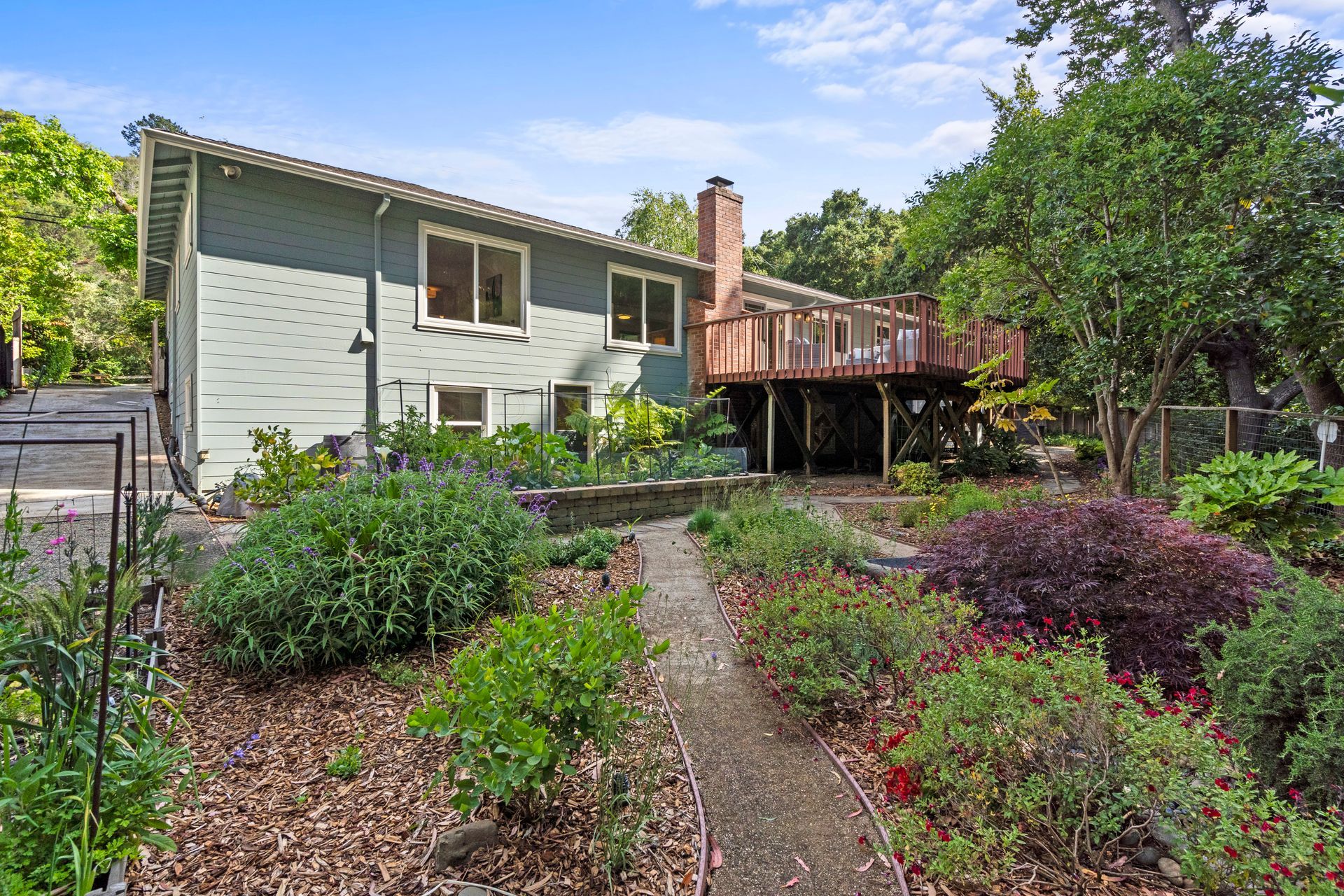 A house with a deck is surrounded by a lush green garden.