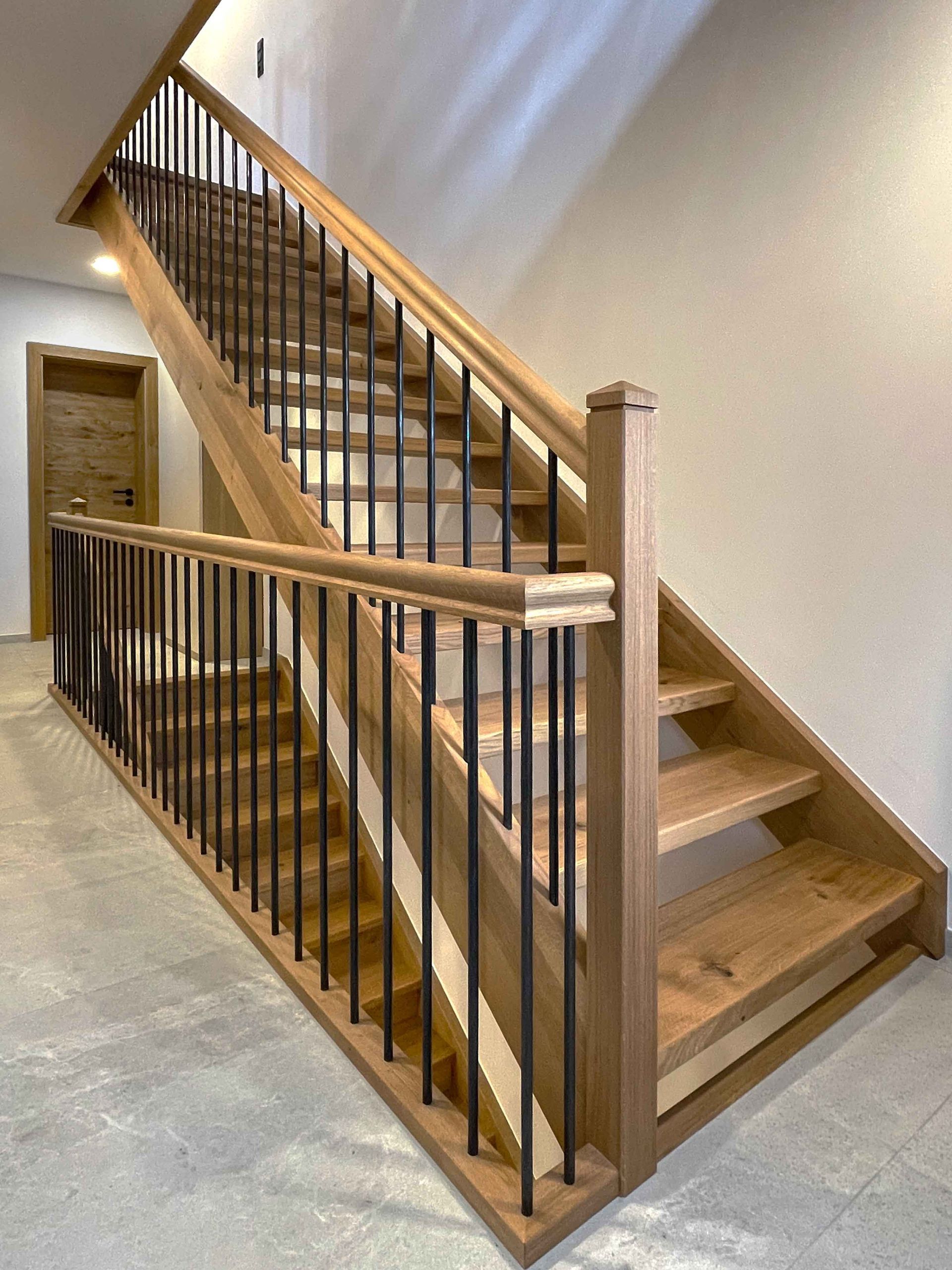 Holztreppe mit schwarzen Metallgeländern und ein mit Teppich ausgelegter Treppenabsatz in einem modernen Interieur.