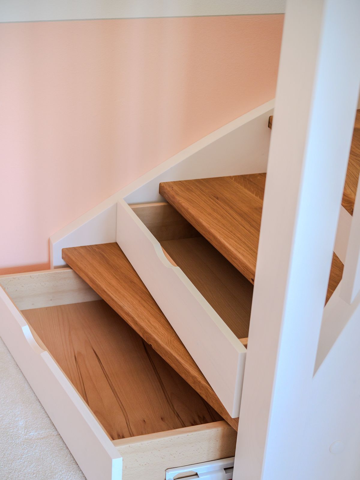 Holztreppe mit weißem Geländer und hellrosa Wand.