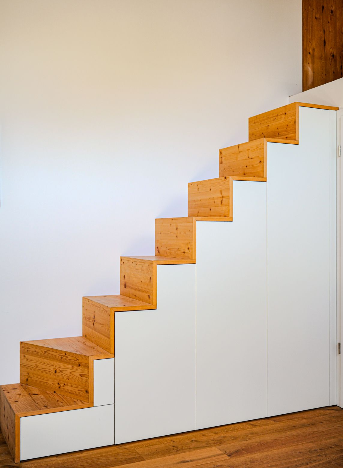 Holztreppe mit weißen Seitenpaneelen in einem minimalistischen Interieur