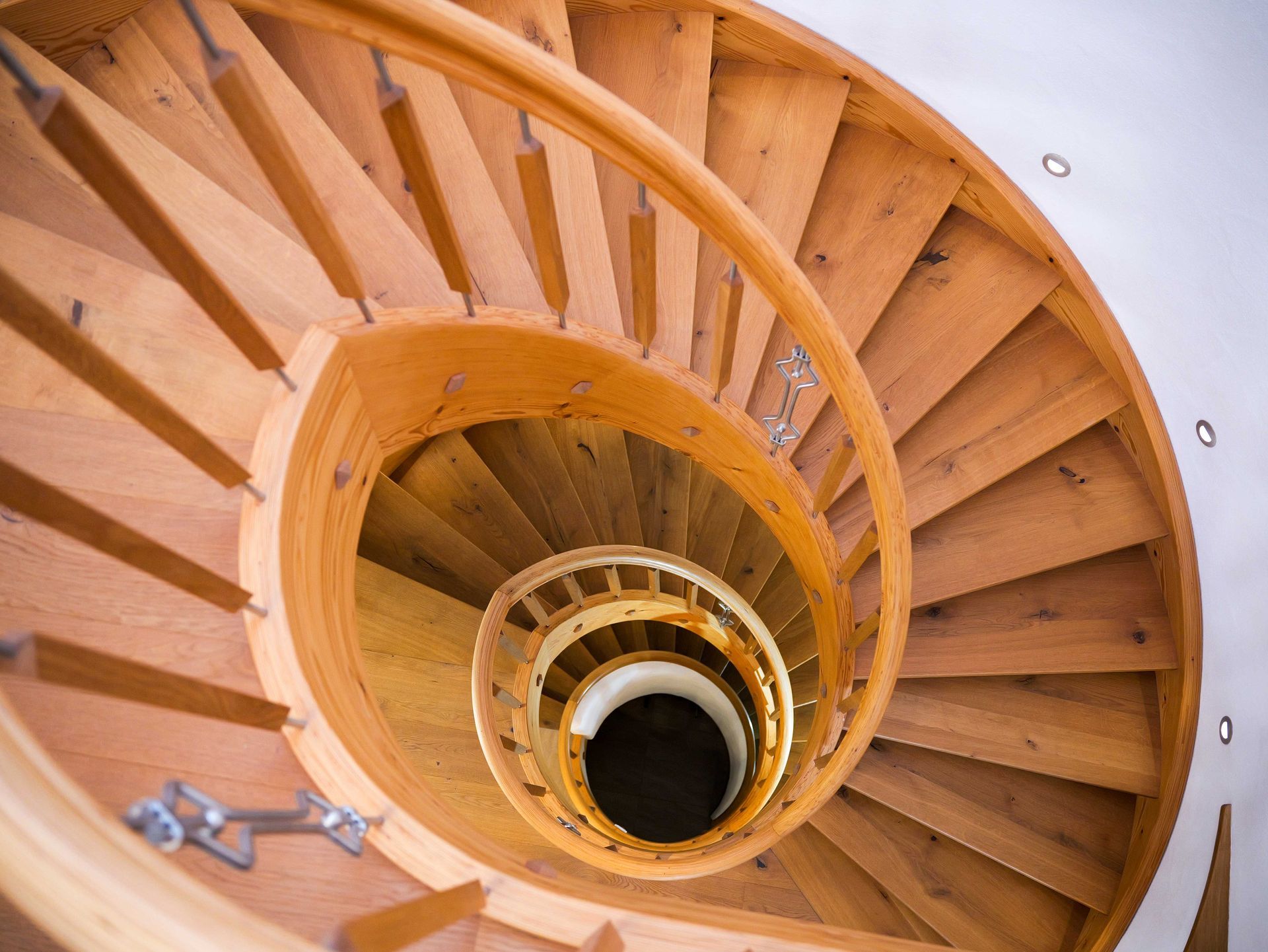 Blick hinunter auf eine spiralförmige Holztreppe mit orangefarbenen Stufen und Geländern um eine zentrale Öffnung