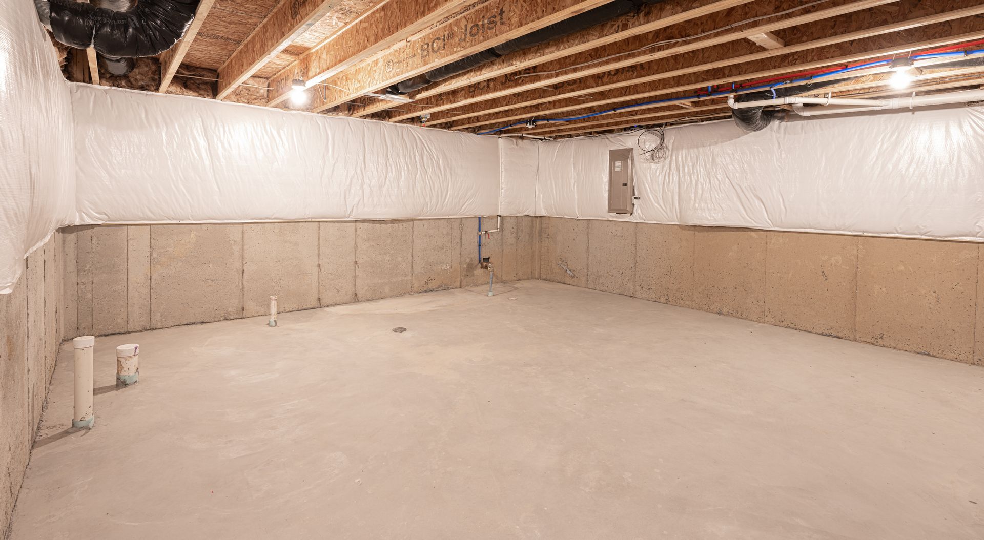 Empty unfinished basement with exposed ceiling joists, white insulation, and concrete floor
