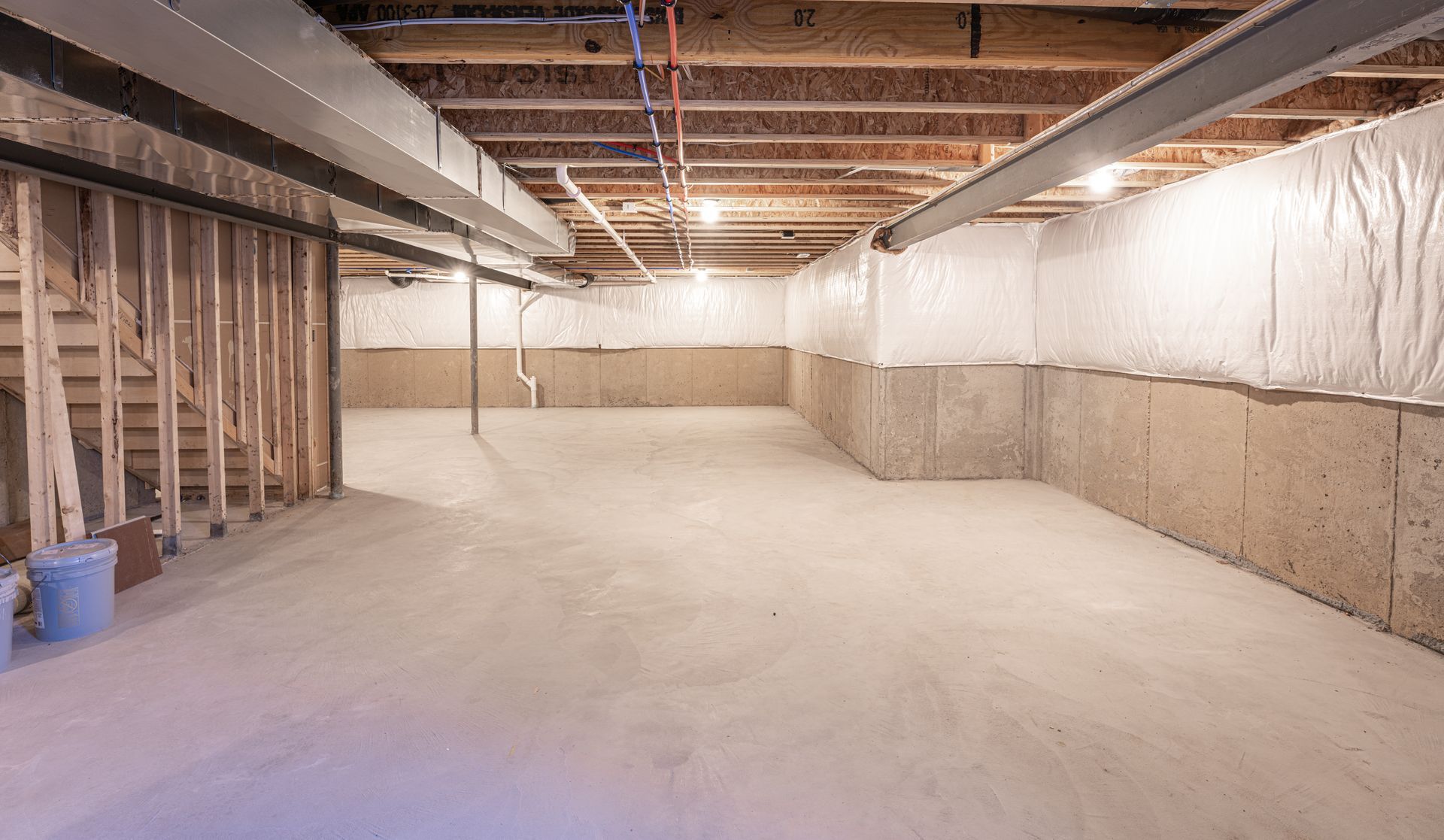 Empty basement under construction with exposed joists, insulation, and concrete floor Empty basement under construction with exposed joists, insulation, and concrete floor